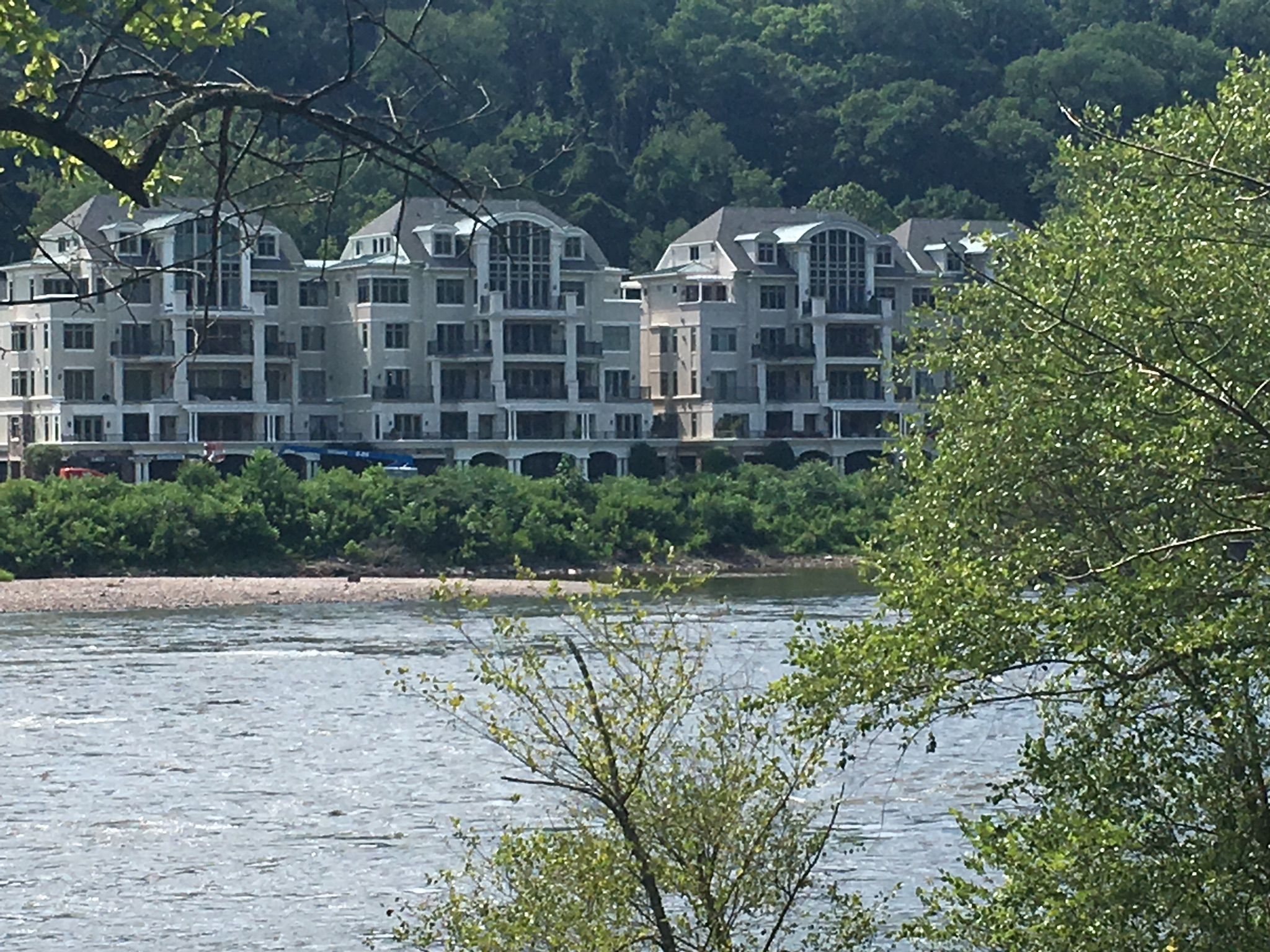 A large building overlooks a wide river with lush green trees. - New Hope-Lambertville Bridge loop from Howell Living History Farm