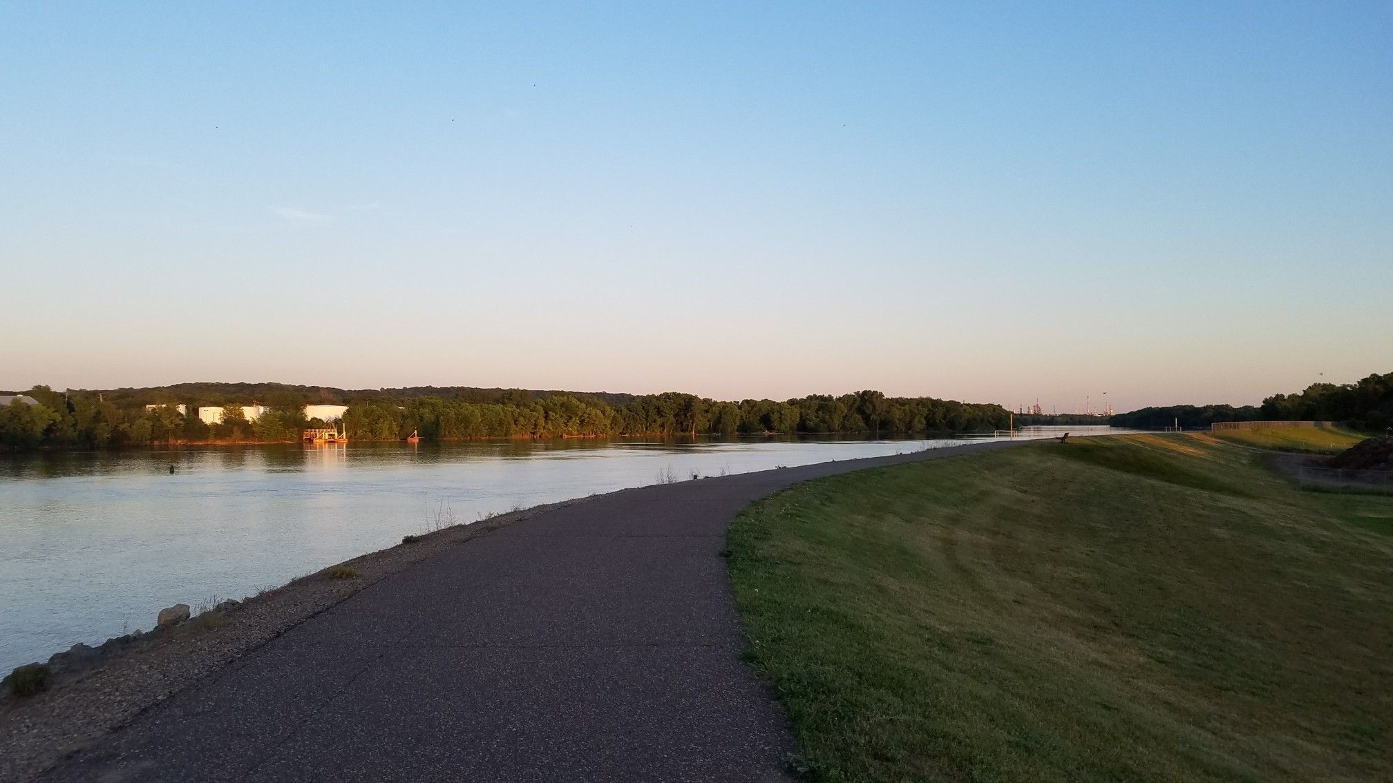 Paved path and grassy bank next to a wide river at sunset. - Wakota Trailhead loop from Saint Paul Park