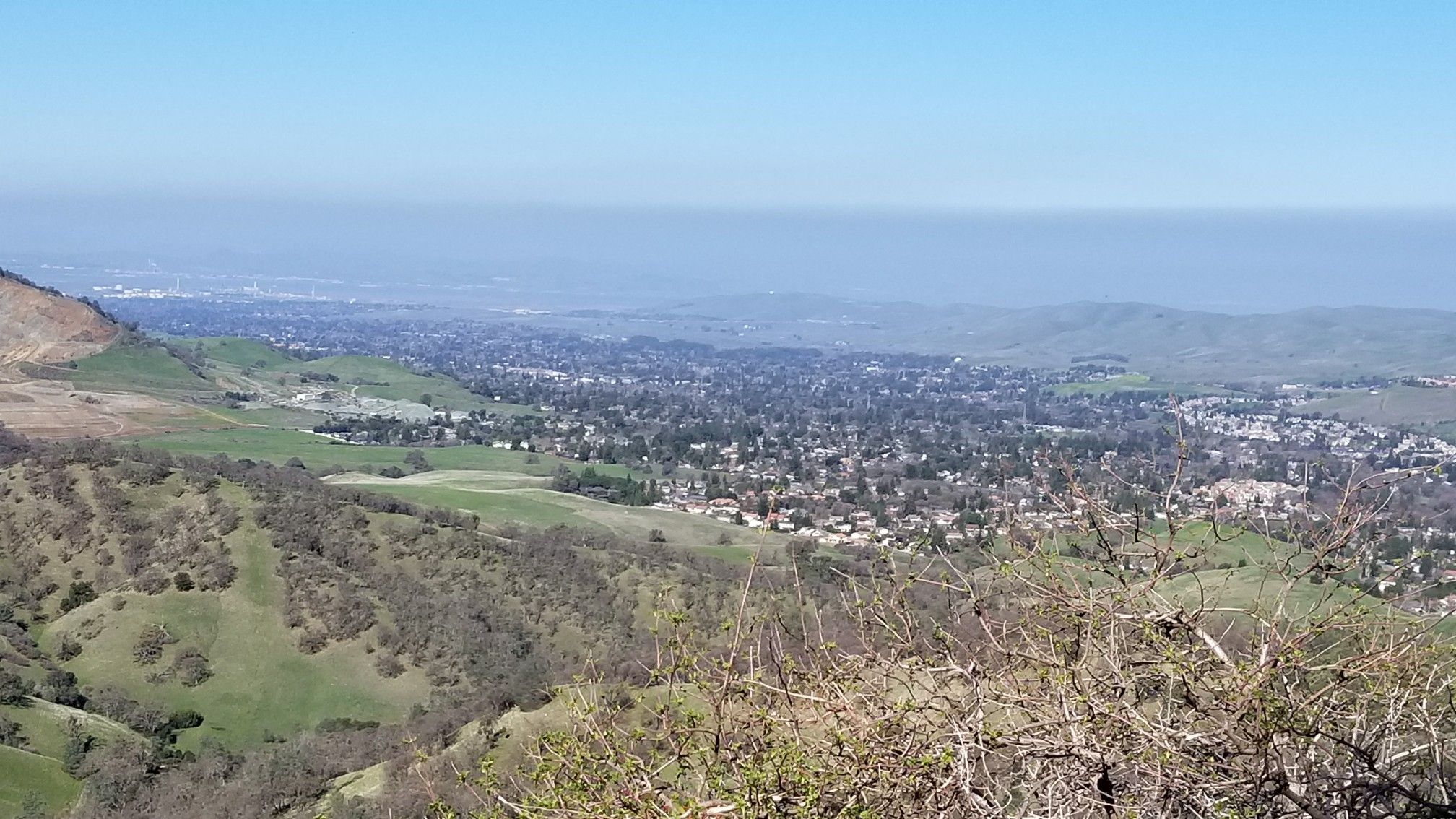 Wide view of a valley town nestled among green hills under a hazy sky. - Donner Canyon Road – Mount Olympia loop from Lot 25