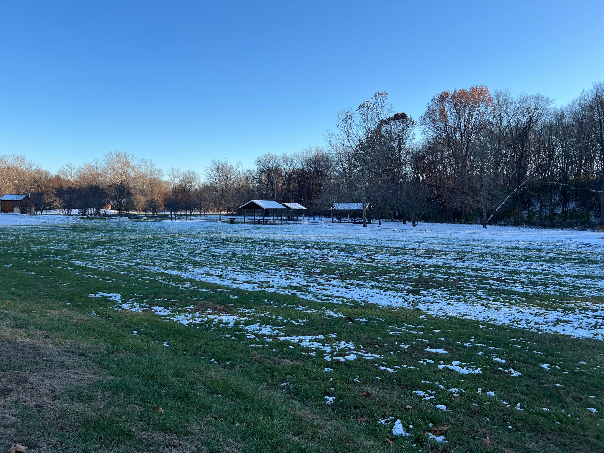 Sunny winter landscape with snow-dusted field, bare trees, and shelters. - Cattle Ridge Trail