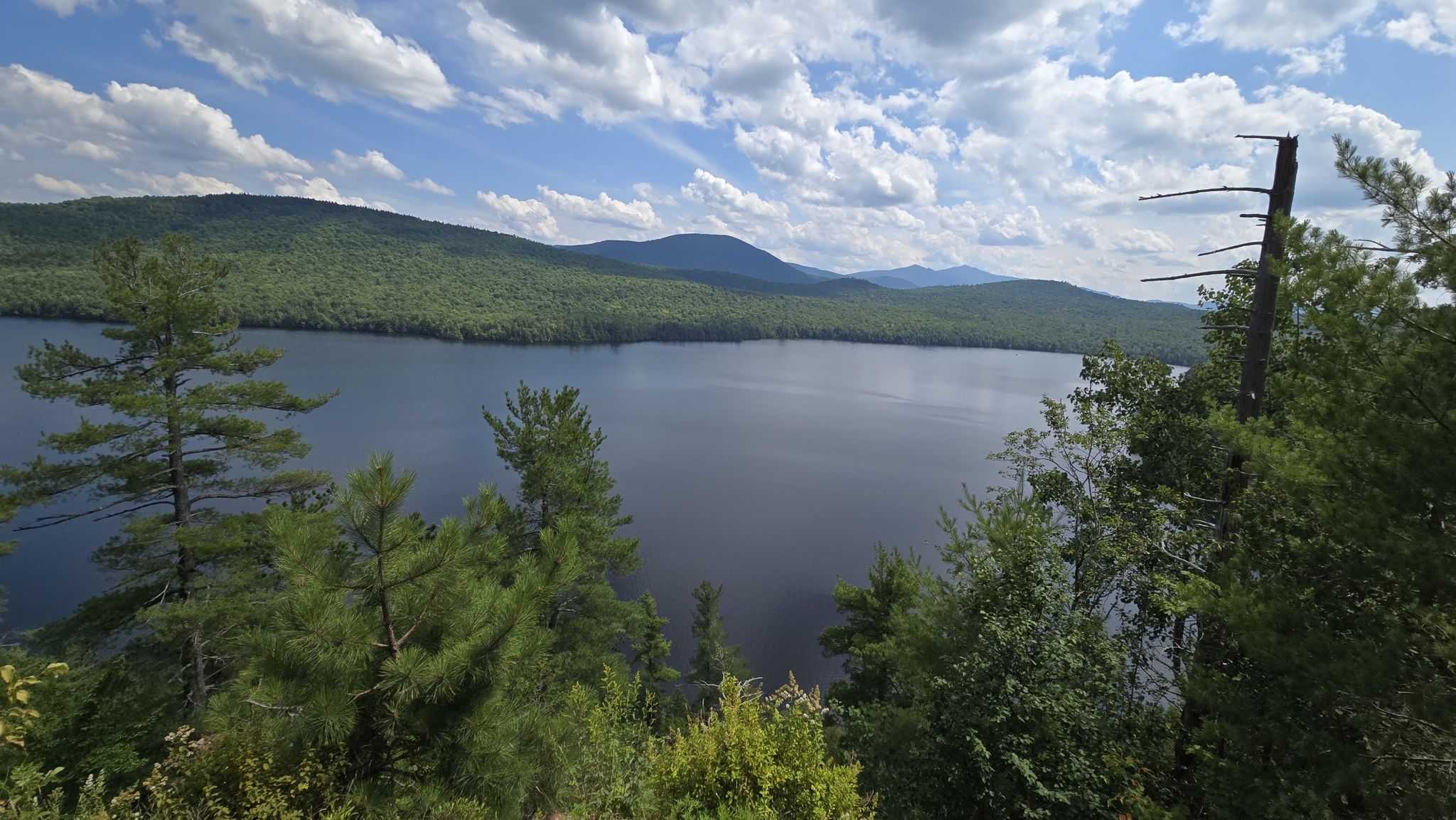 Panoramic view of a large lake surrounded by forested mountains under a cloudy sky. - Silver Lake Bog Preserve Trail