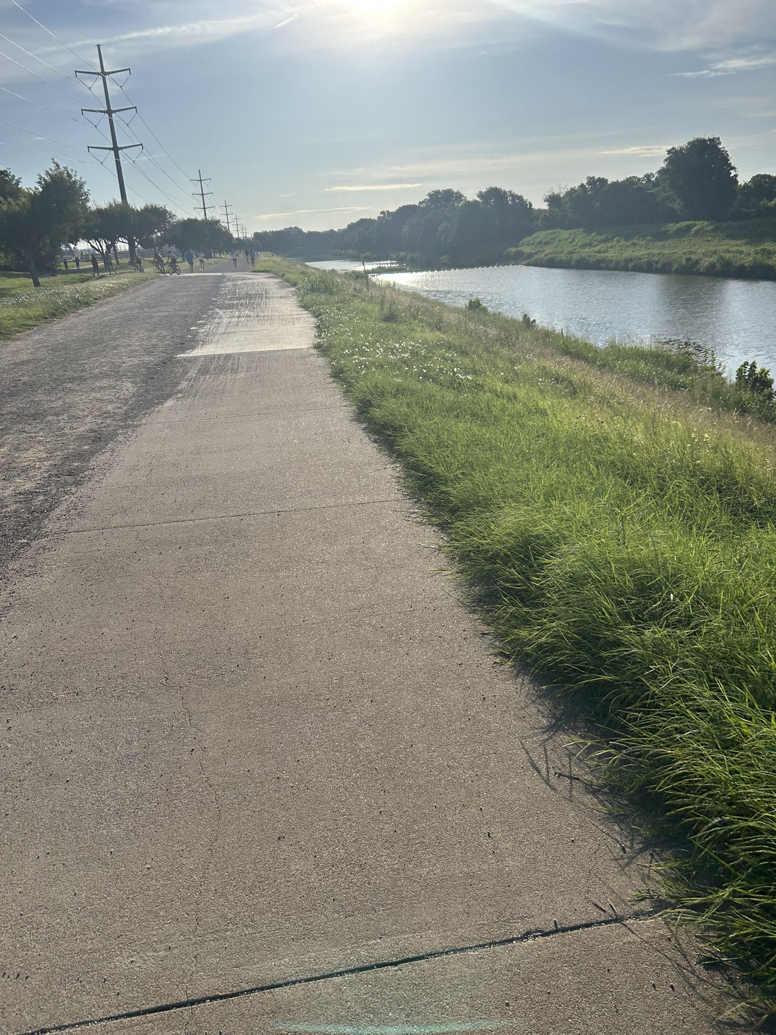 Paved path next to a river with green banks under a bright sky. - Johnny's Bike Shop – Trail along the Trinity river loop from The Shops at Clearfork