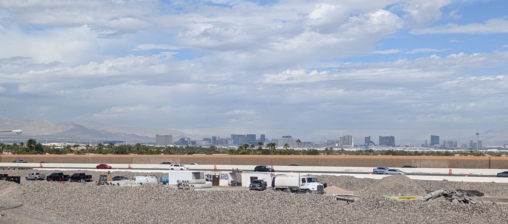 A highway with vehicles, construction, and a distant city skyline under clouds. - Harry Reid UPRR and Pittman Wash Trails Loop