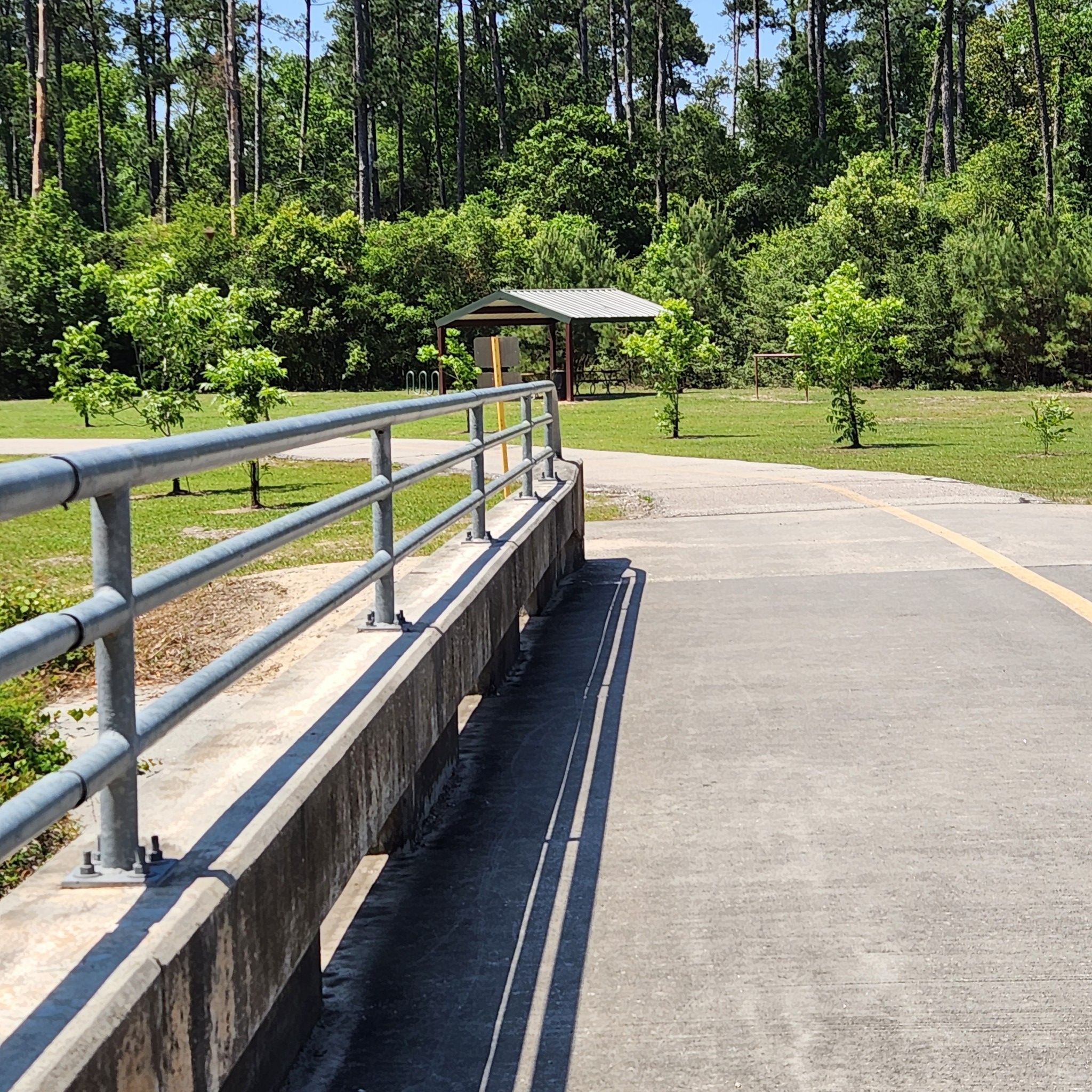 Concrete bridge with metal railings, leading to a grassy park with a shelter. - Spring Creek Greenway loop from Bibi and Mini-Me Bush Dog Park