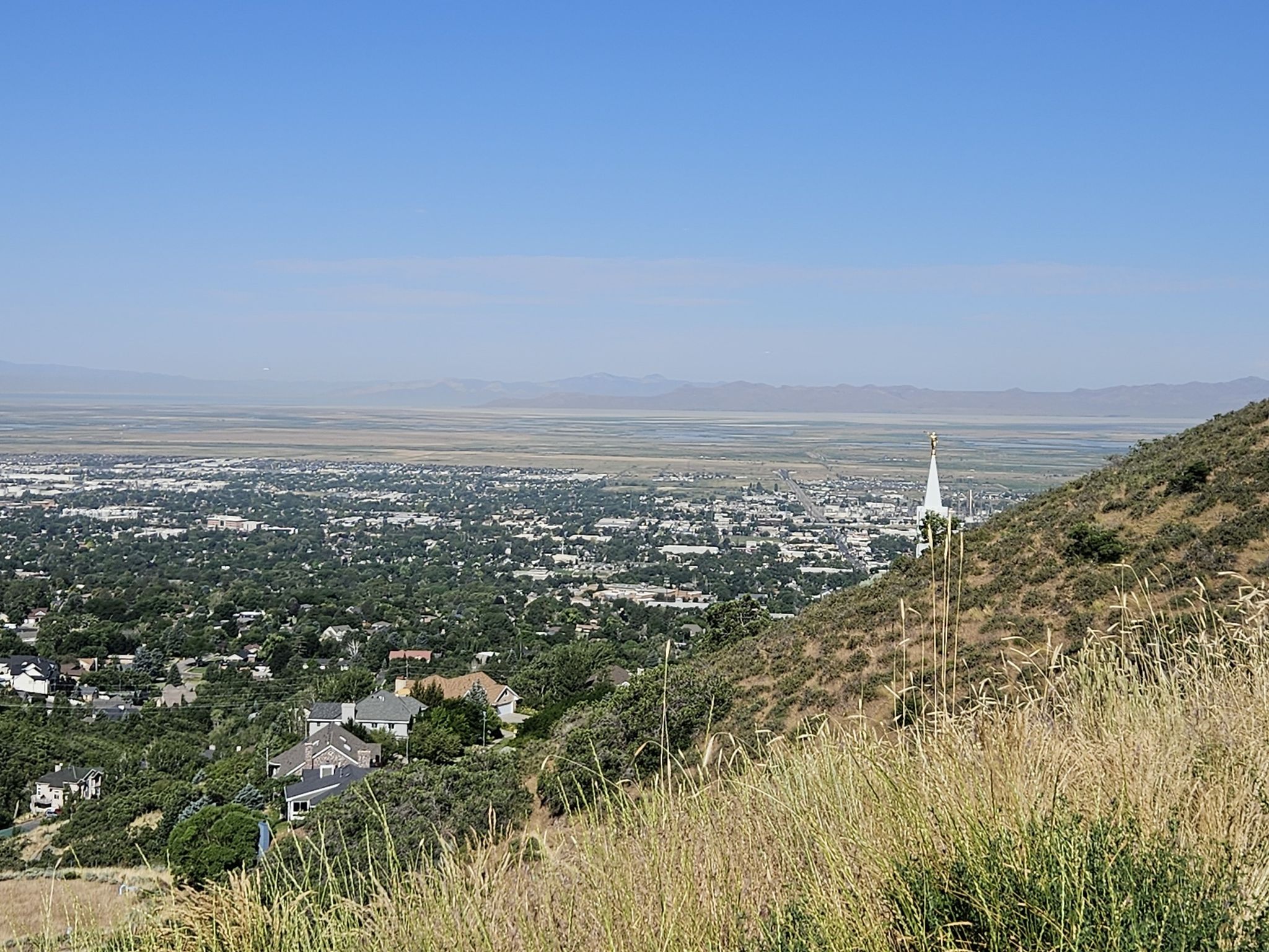 City and valley vista from a grassy hillside, with a white spire. - Temple Loop