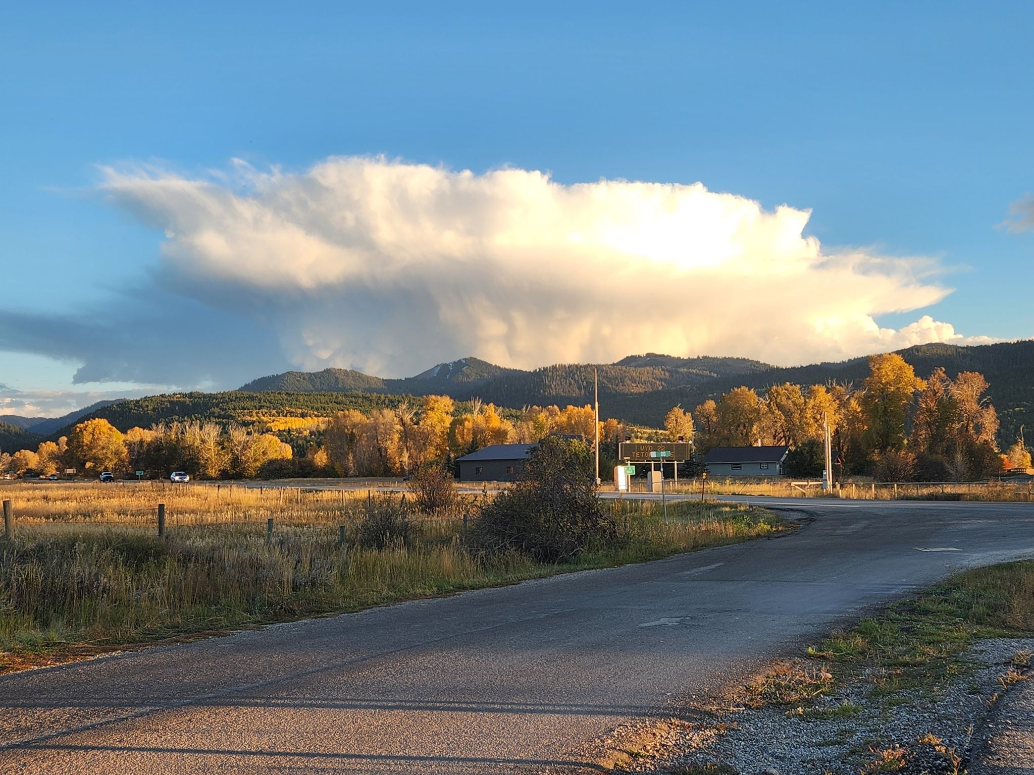 A road leads past buildings and golden trees, under a large cloud. - South Victor Bike Path Loop