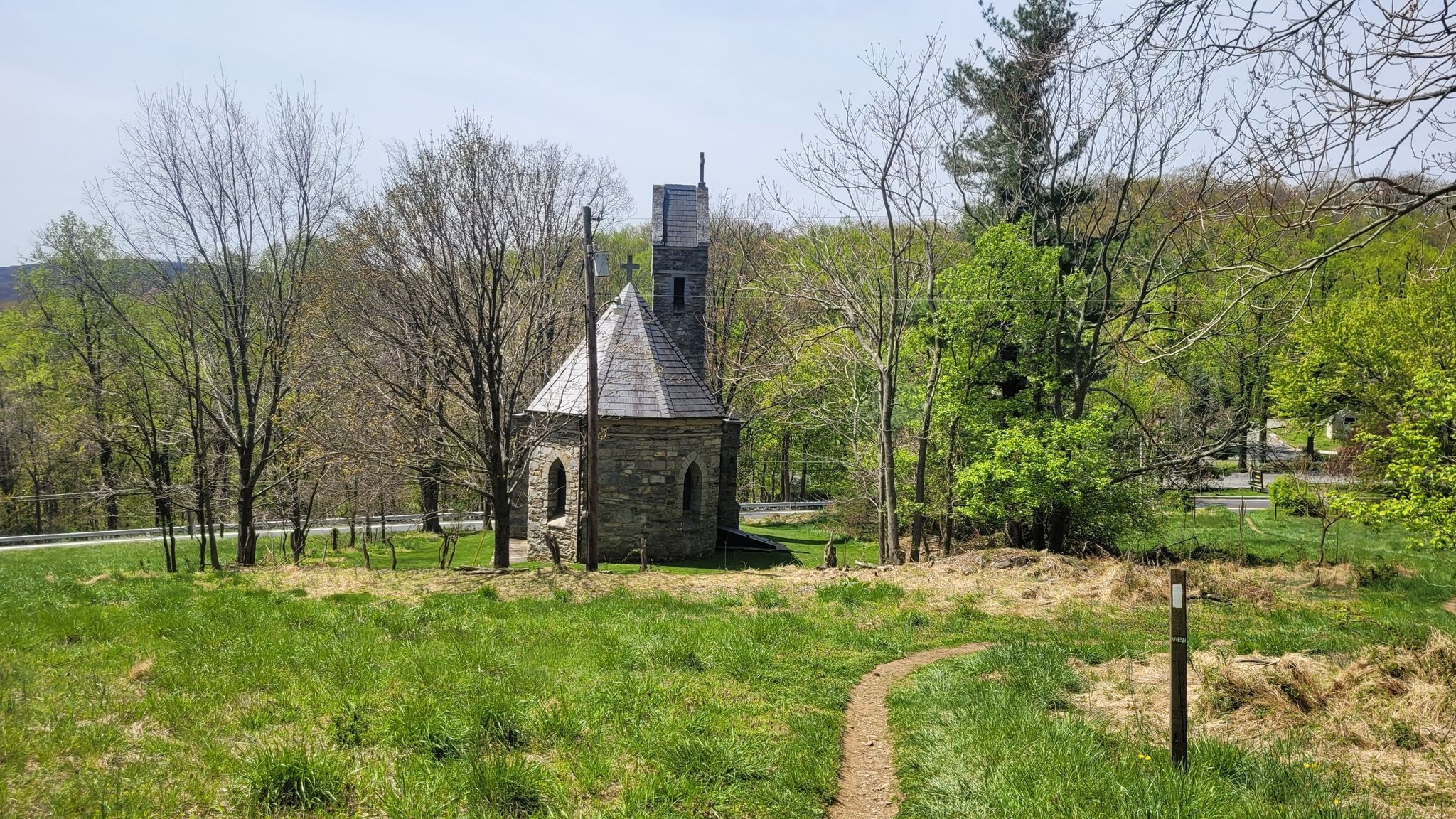 Small stone chapel with a tower stands in a sunny, grassy field. - Appalachian National Scenic Trail