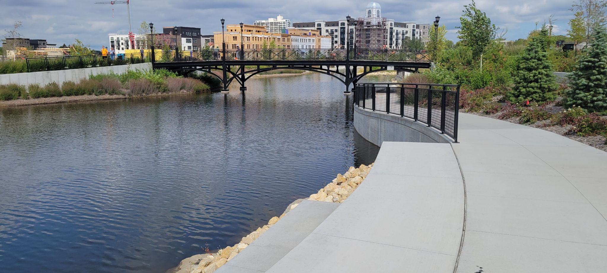 River with a bridge, modern buildings, and a paved path under cloudy sky. - Minnehaha Falls Loop
