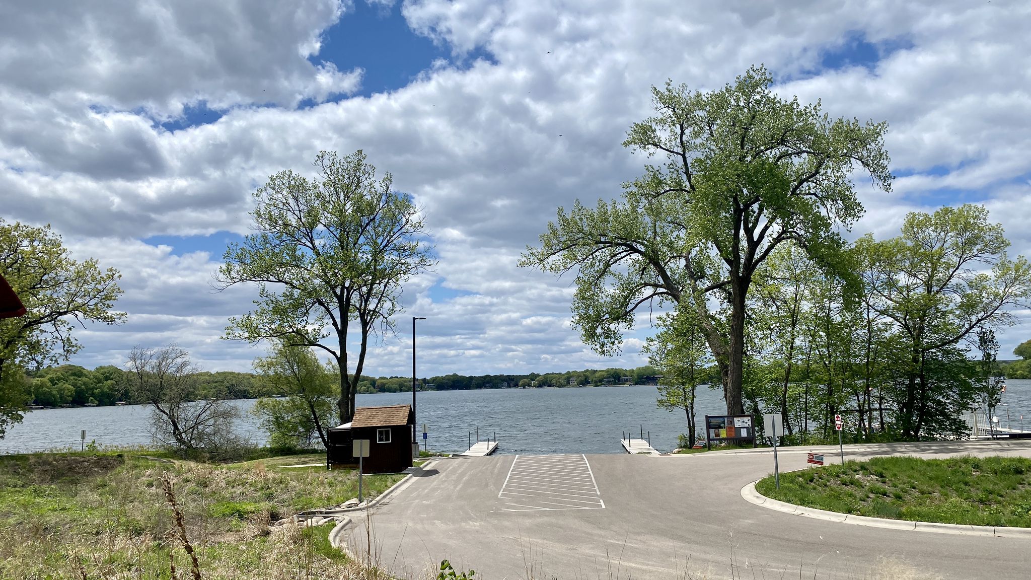 Boat launch area with a small building by a large lake, cloudy sky. - Riley Lake Park – Saint Albans Bay Bridge loop from Deephaven