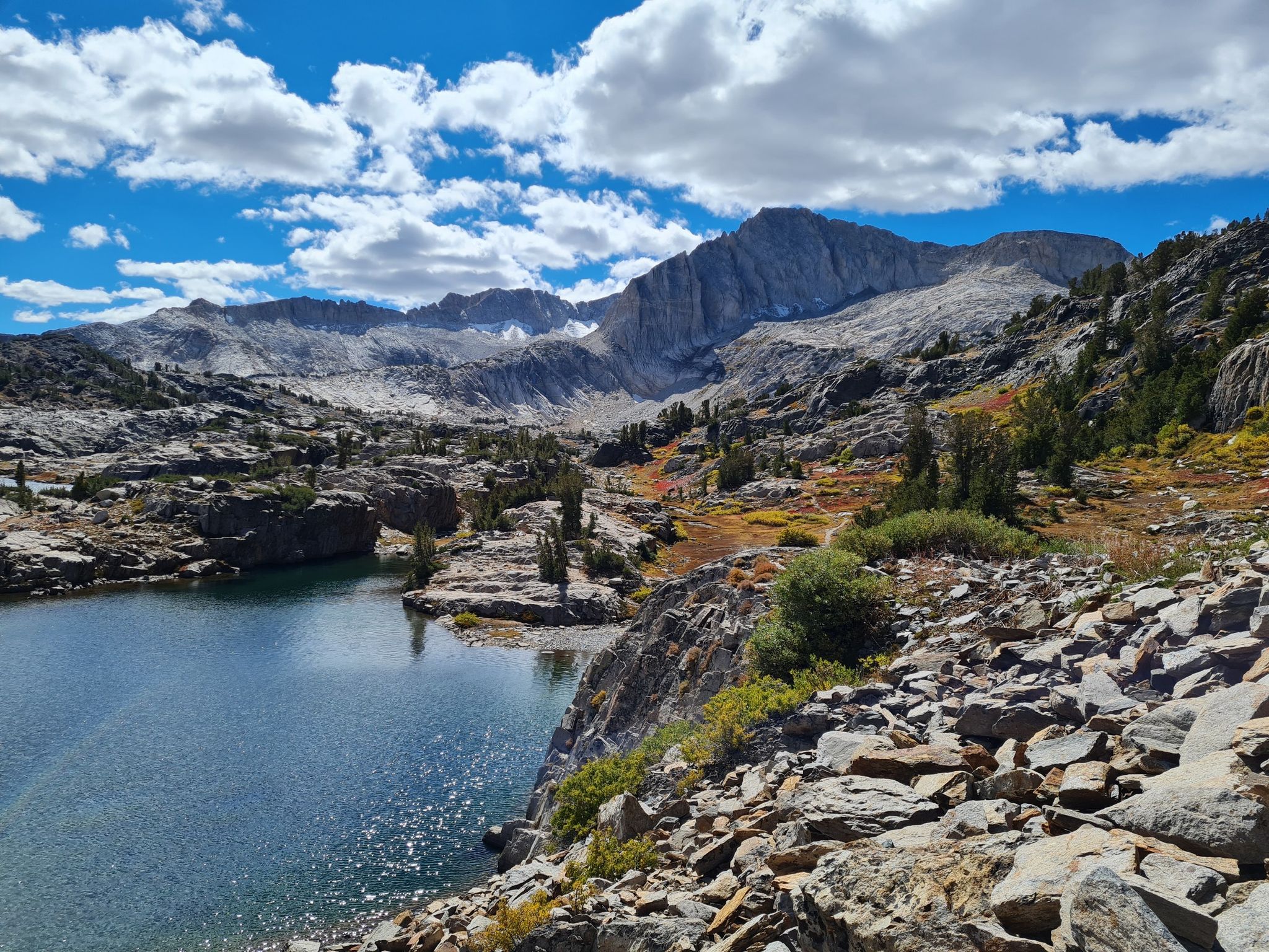 Alpine lake with rocky shores, distant mountains, and a partly cloudy sky. - Twenty Lakes Basin Loop