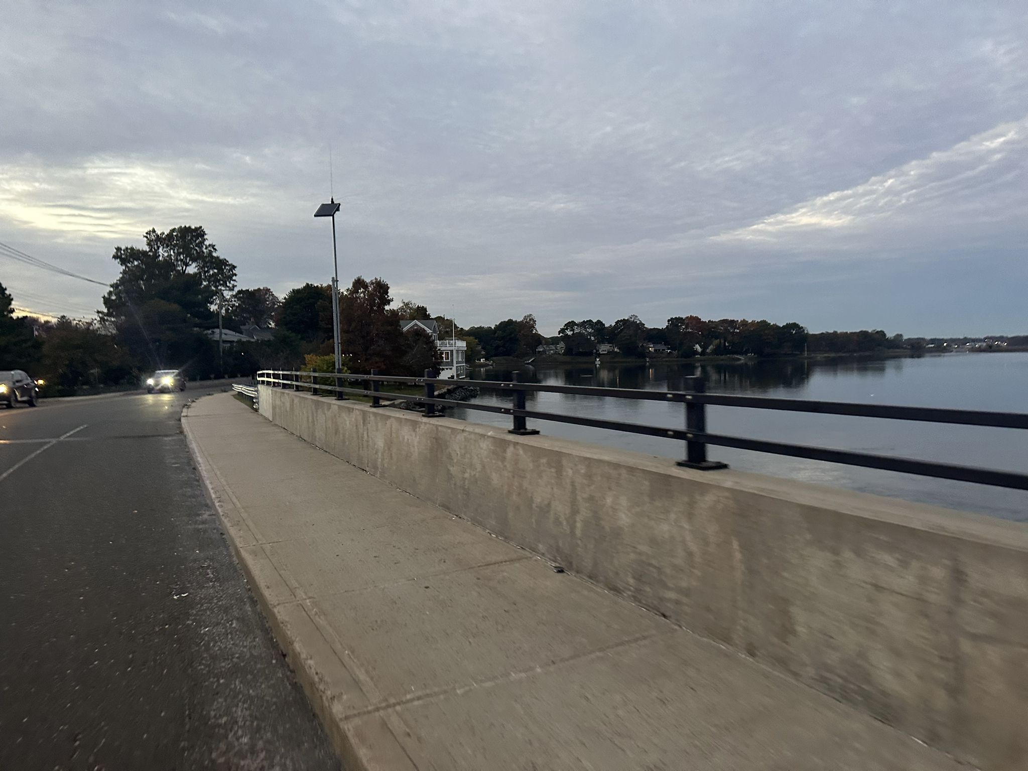 A concrete bridge and sidewalk next to a calm body of water at dusk. - Knobb Hill loop from Silver Sands State Park