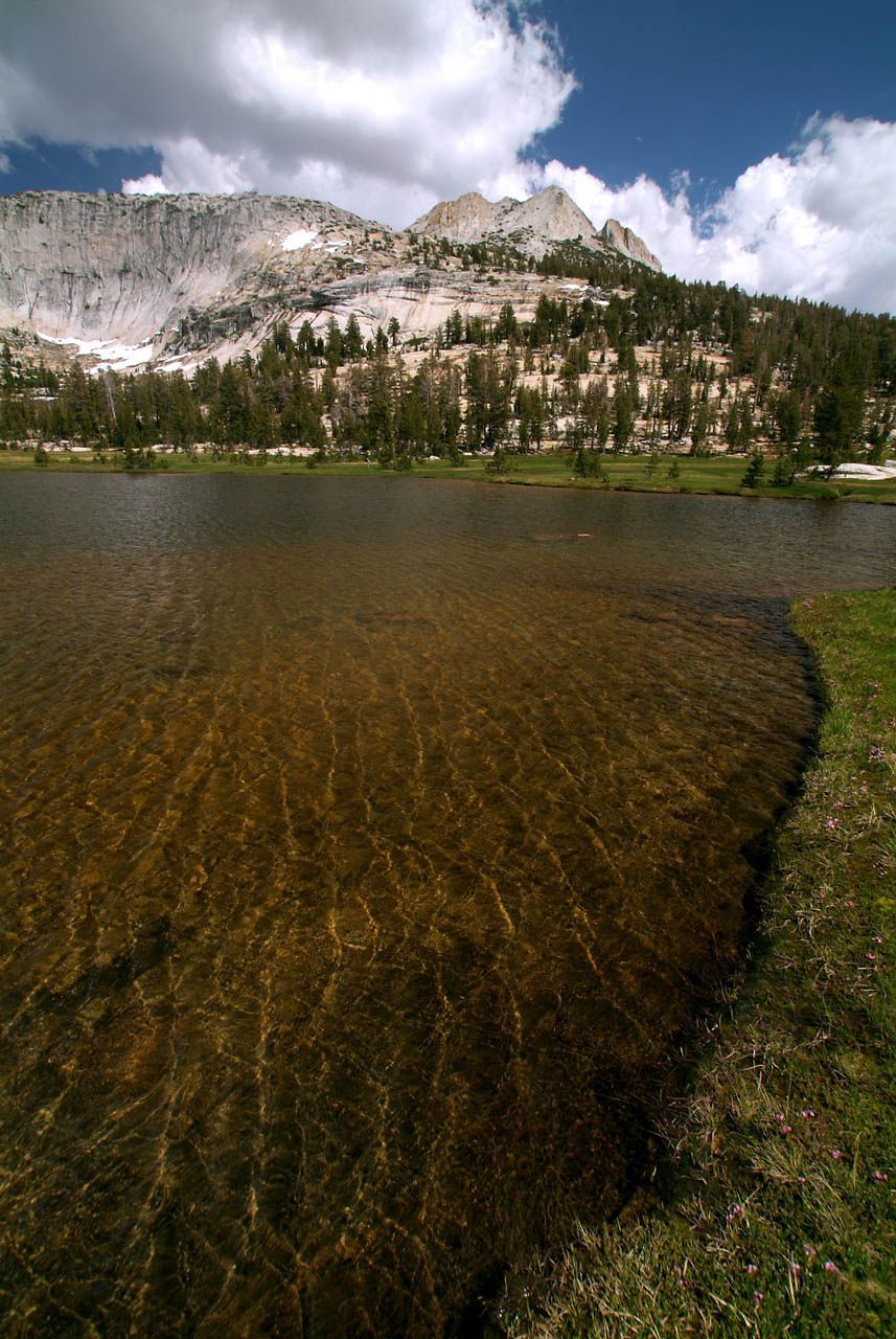 Clear lake reflecting mountains and trees under a partly cloudy sky. - Cathedral Lakes Trail