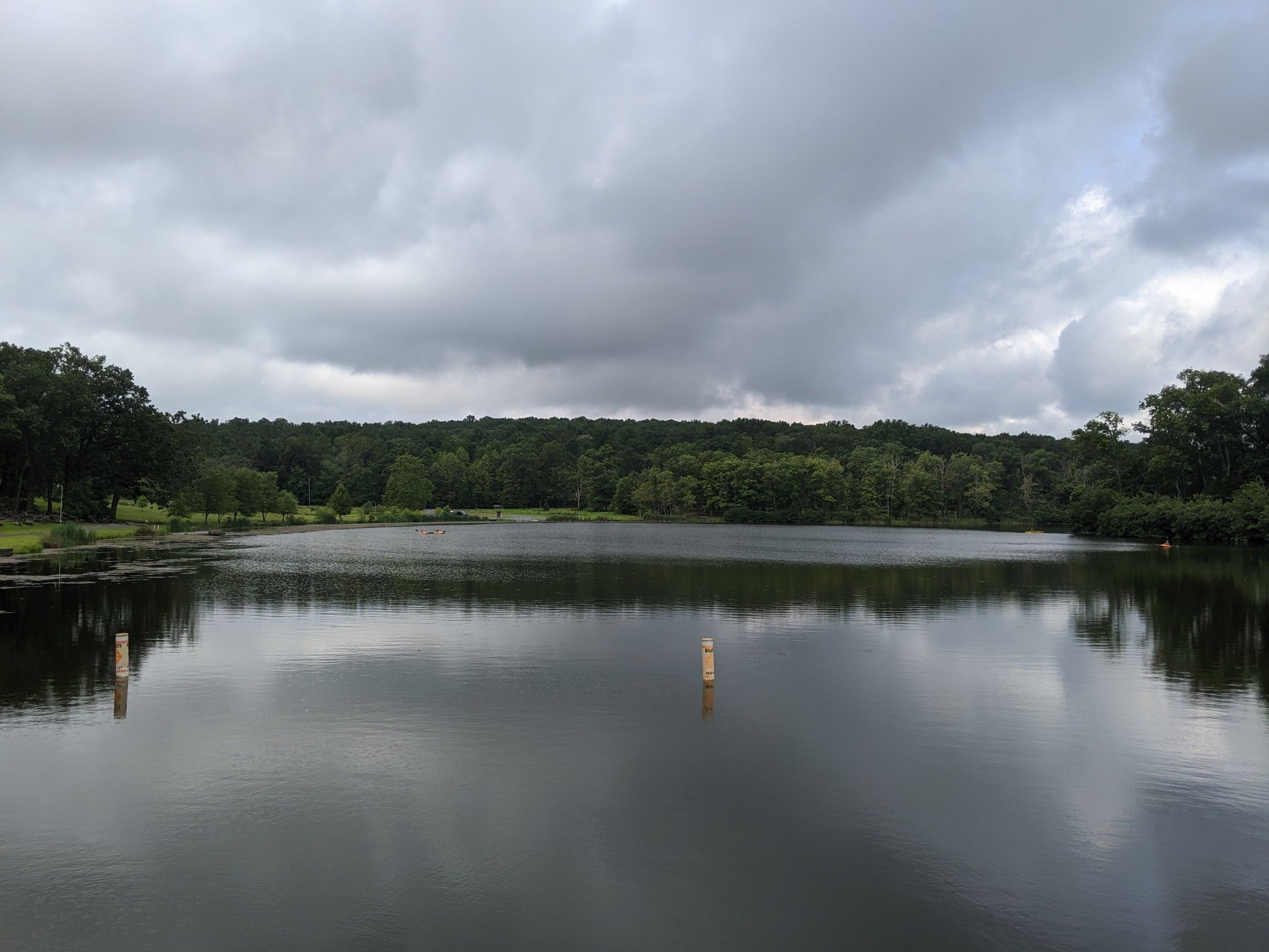 Calm lake with two buoys, surrounded by green trees under a cloudy sky. - Perkiomen Bicycles – Deep Creek Lake loop from Green Lane