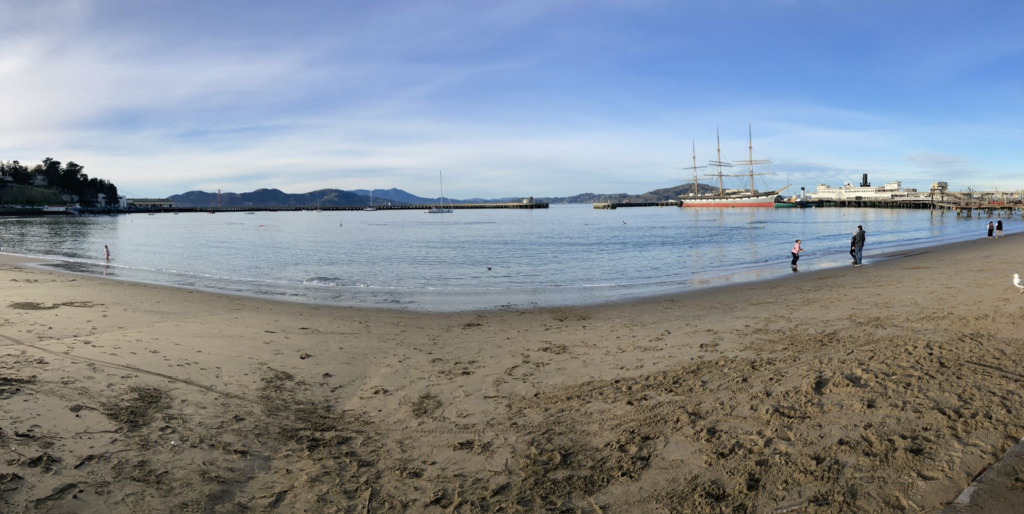 Sandy beach leading to a bay with distant ships and mountains, people walking. - San Francisco Bay Trail: The Embarcadero