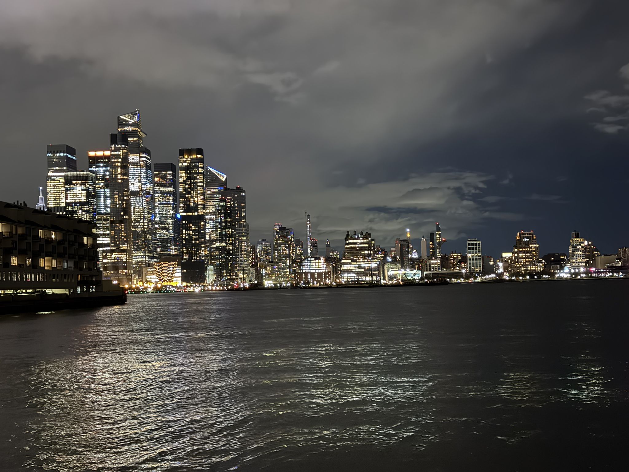 Illuminated city skyline across dark water at night under cloudy sky. - Weehawken Cove loop from Hoboken