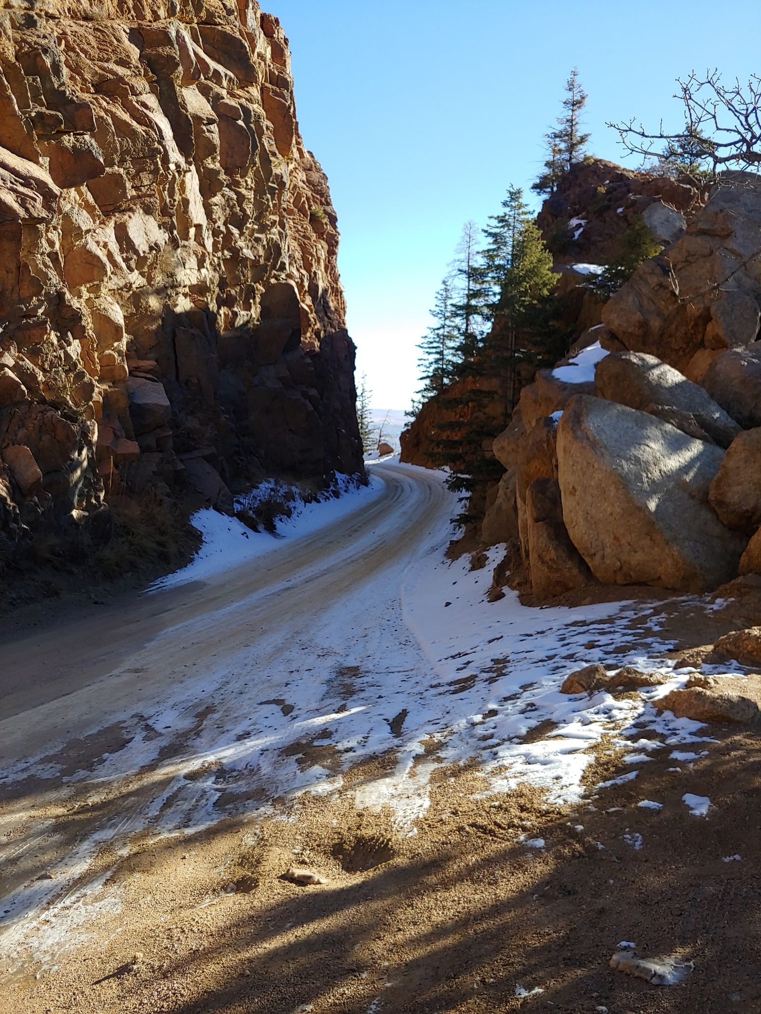 Snow-dusted dirt road winding through a narrow, sunny canyon with tall rock walls. - Cripple Creek from Colorado Springs on the Gold Camp Road