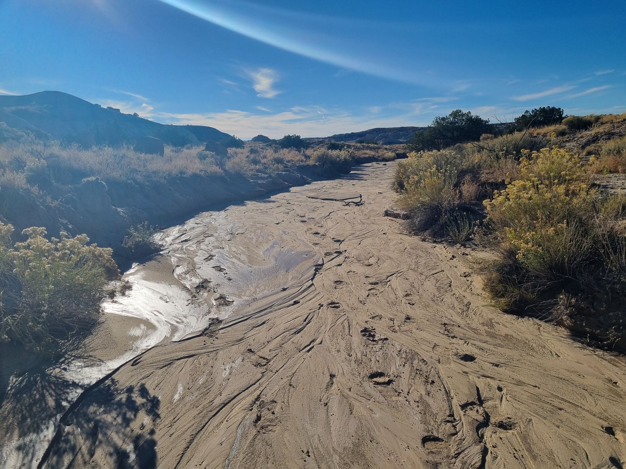 Dry sandy wash with ripples, surrounded by desert hills under a bright sky. - De Na Zin Wilderness Trail