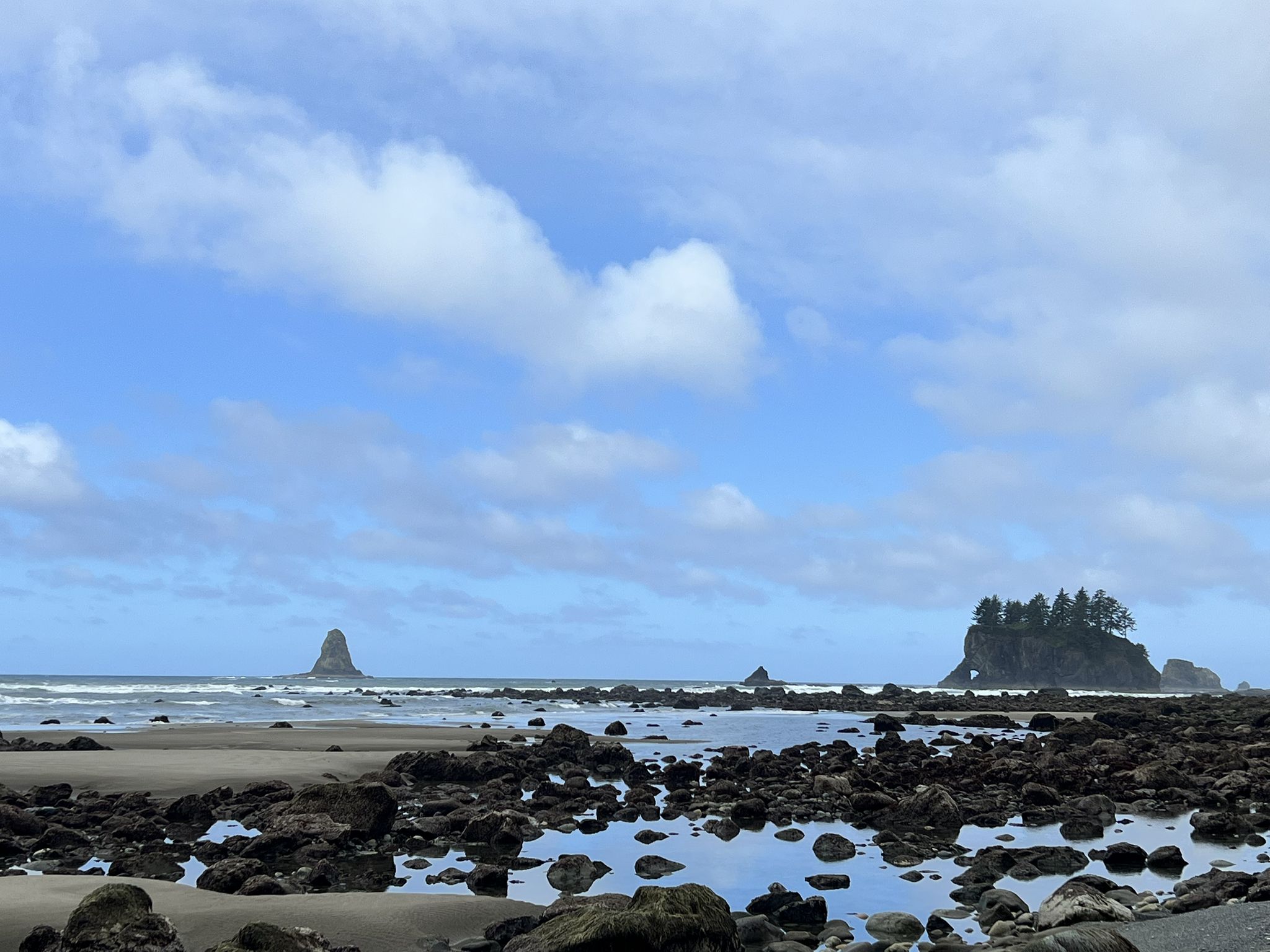 Sunny rocky tide pools and sandy beach with distant sea stacks and ocean. - Hiking loop from Point of Arches State Park Property