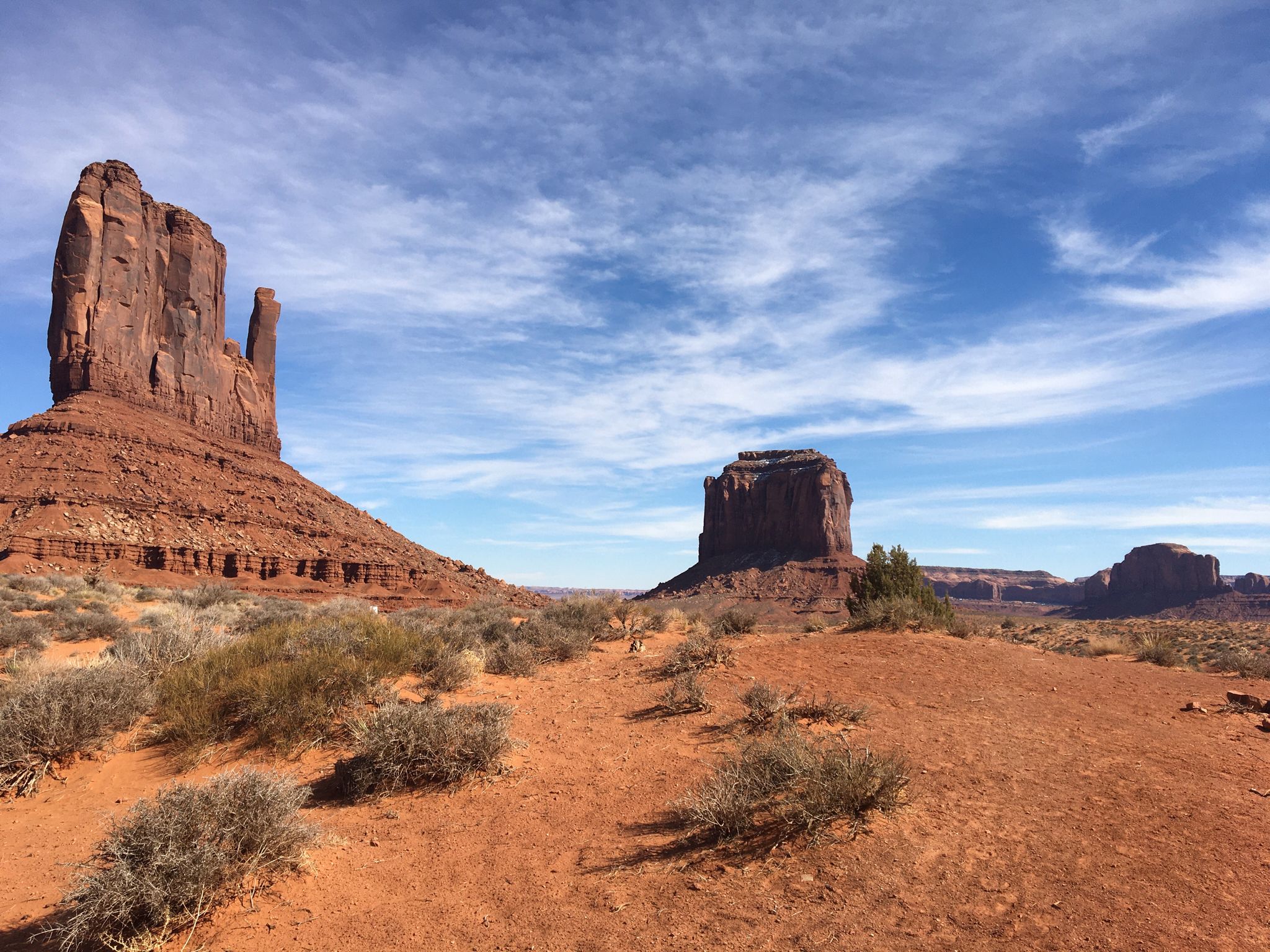 Two large red rock formations in a desert landscape under a blue sky with clouds. - Hiking loop from Monument Valley Navajo Tribal Park