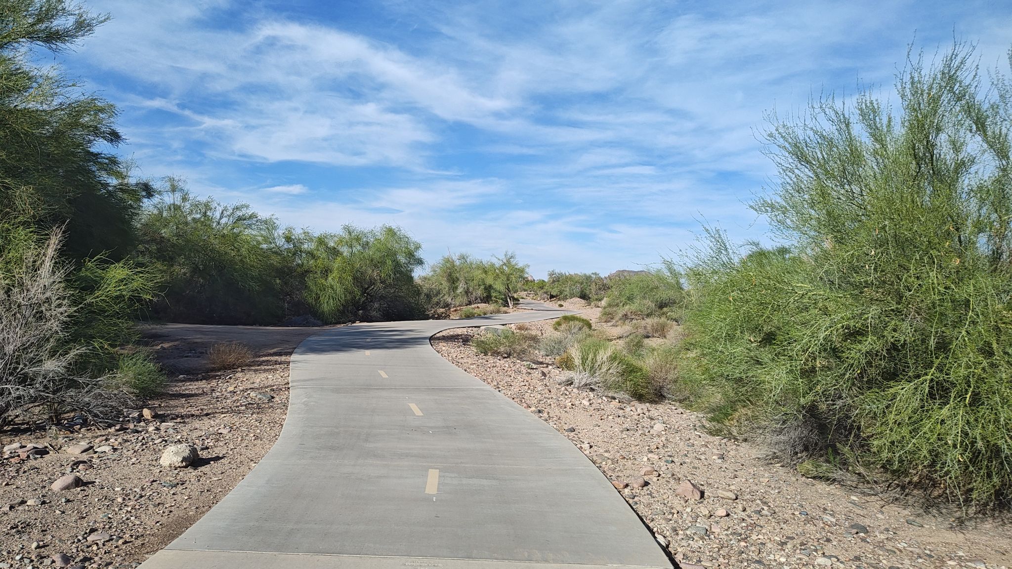 Winding paved path through desert scrub and bushes under a partly cloudy sky. - Dawn Lake loop from Sierra Verde Elementary School