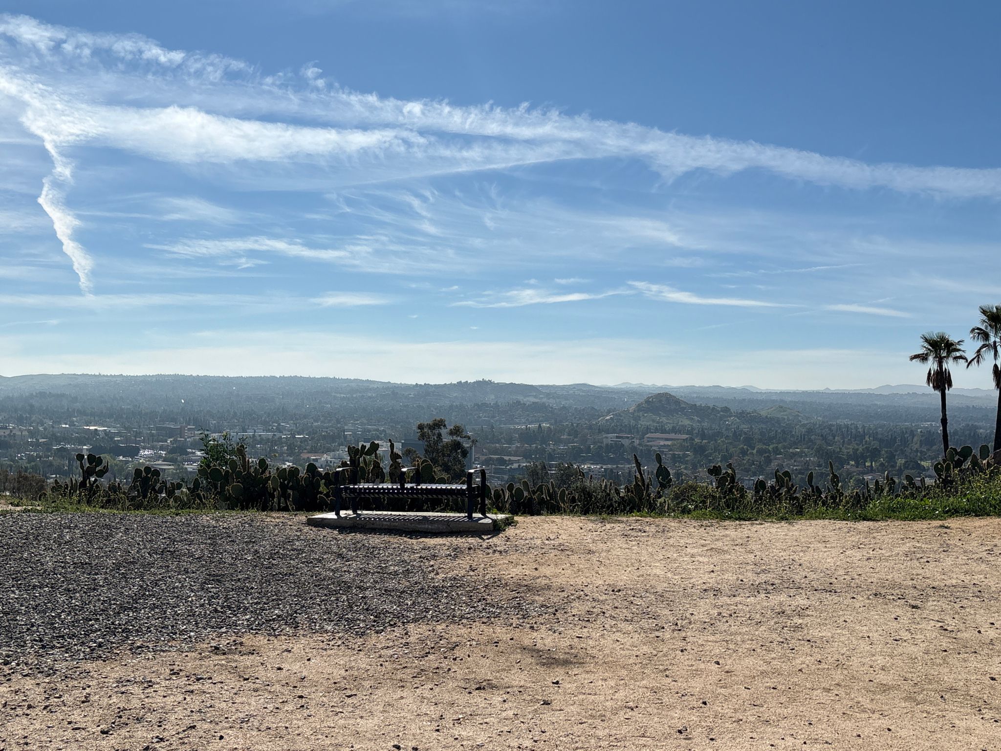A park bench overlooks a vast valley and distant city under a bright sky. - Mount Rubidoux Loop