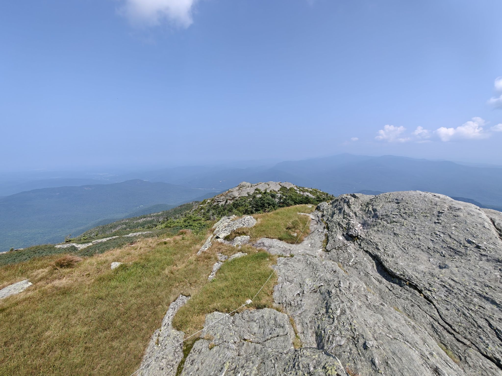 Rocky mountain ridge with sparse grass and distant hazy mountains. - Camel's Hump Summit loop from Forest City Trail