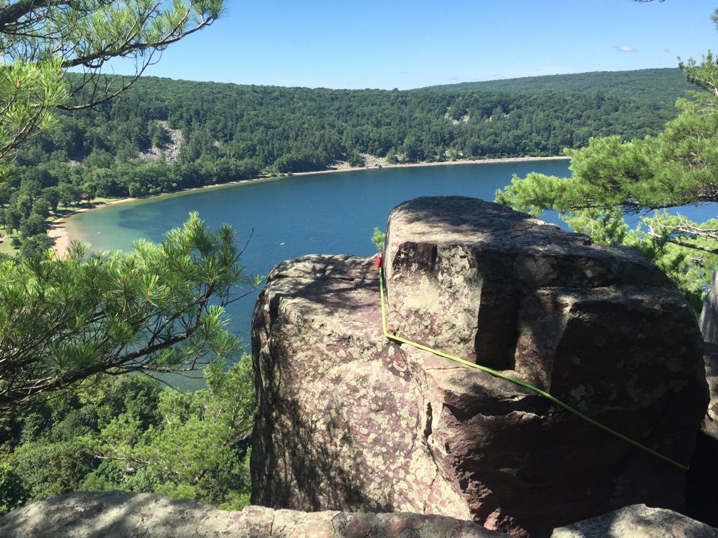 Sunny view of a lake and forest, with a climbing rope on large rocks. - Balanced Rock Trail