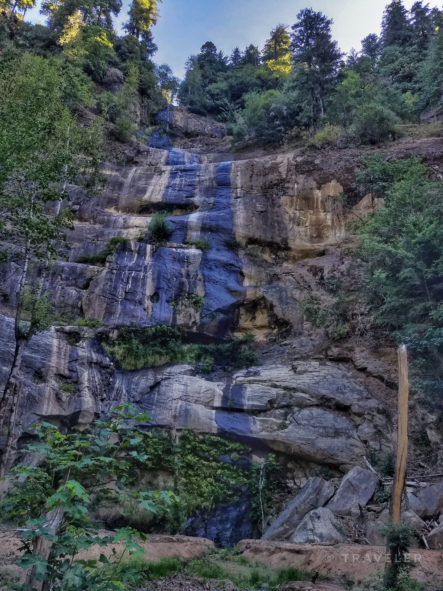 Tall, multi-tiered waterfall cascading down a rocky cliff face in sunlight. - Johnson Mountain gravel loop