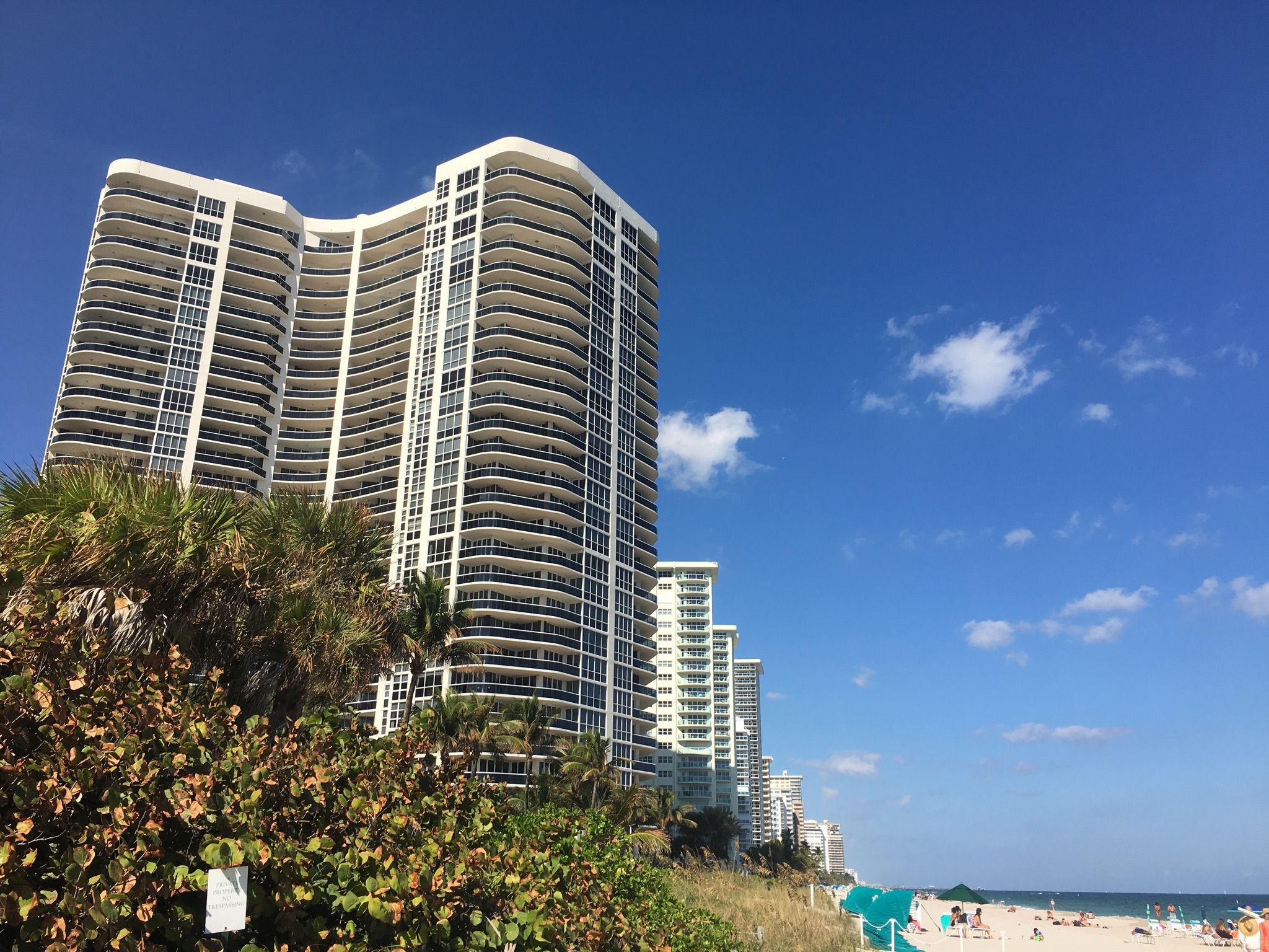Tall white building overlooking a beach with lush greenery under a blue sky. - Earl Lifshey Ocean Park – Plank path along the beach loop from Lauderdale-by-the-Sea