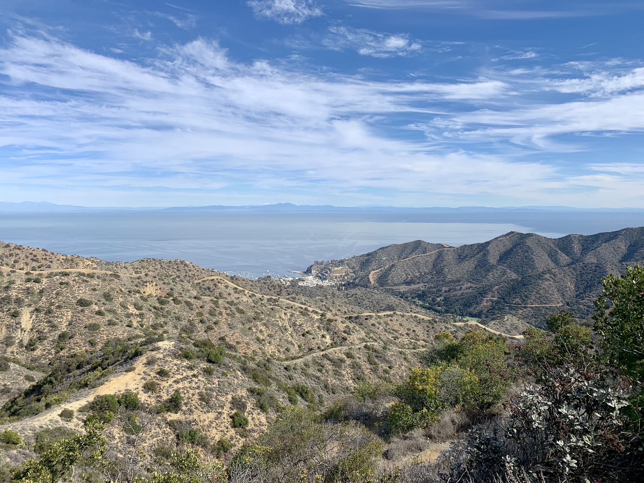 Expansive view of rolling dry hills meeting the ocean under a bright sky. - Hermit Gulch Campground – Trail marker & viewpoint loop from Avalon