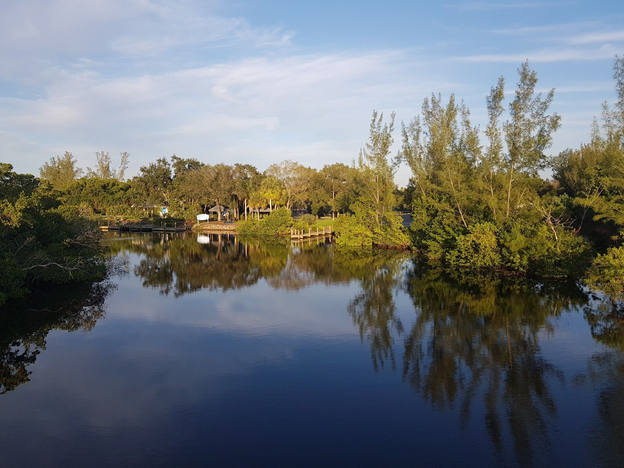 A wide waterway with lush green trees reflecting in the calm water. - Baker Park Boardwalk, Naples – Gordon River Greenway loop from Winding Cypress