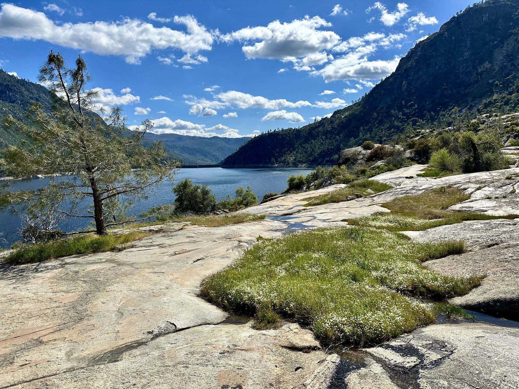 Sunny view of a lake in a valley, with rocky foreground and green patches. - Rancheria Falls Trail