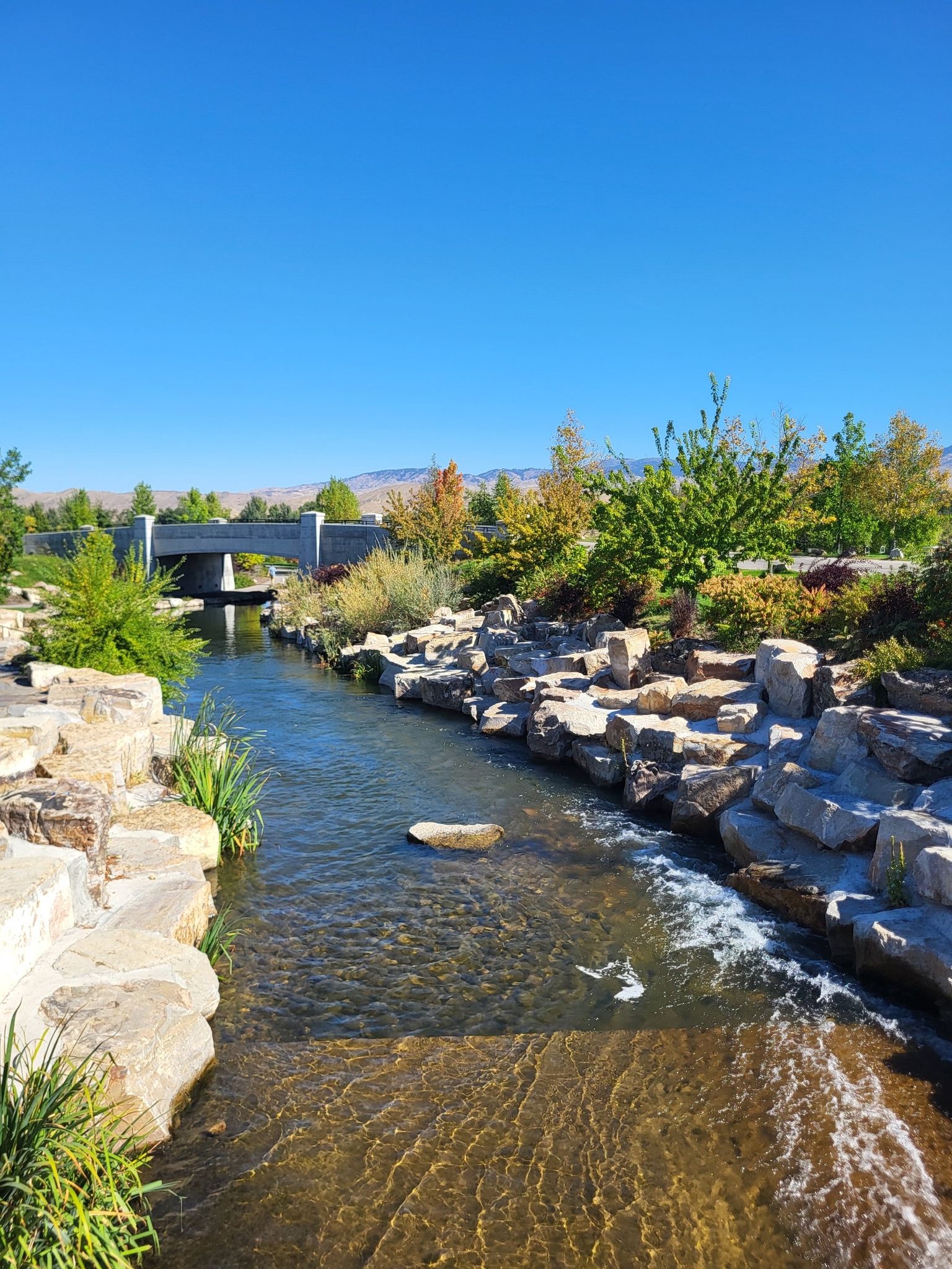 Clear stream flowing through rocky banks under a bright blue sky. - Boise river view – Boise River Greenbelt loop from West Bench Neighborhood Association