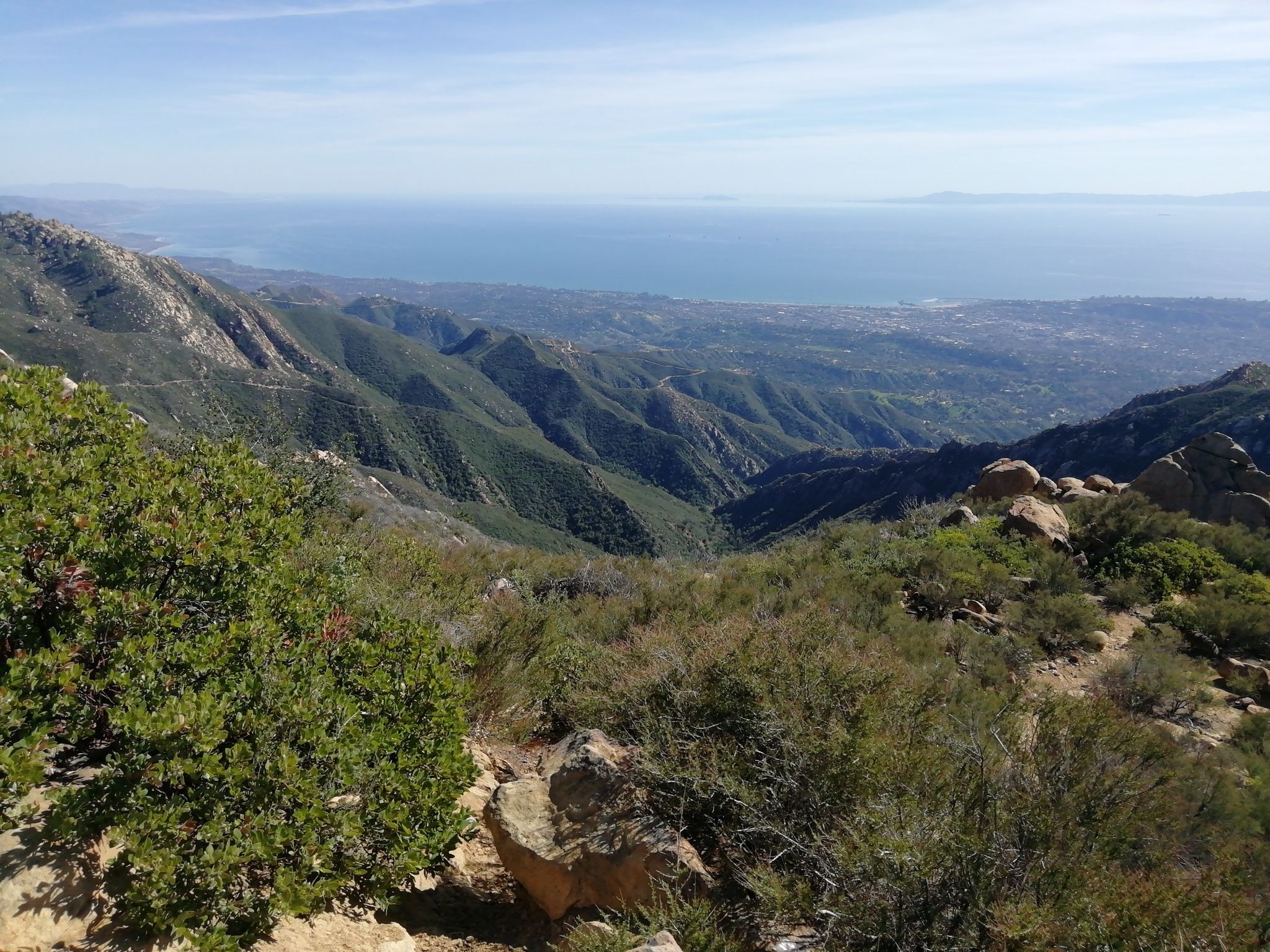 Panoramic view of green mountains, a valley, and ocean under a clear sky. - La Cumbre Peak and Inspiration Point Loop