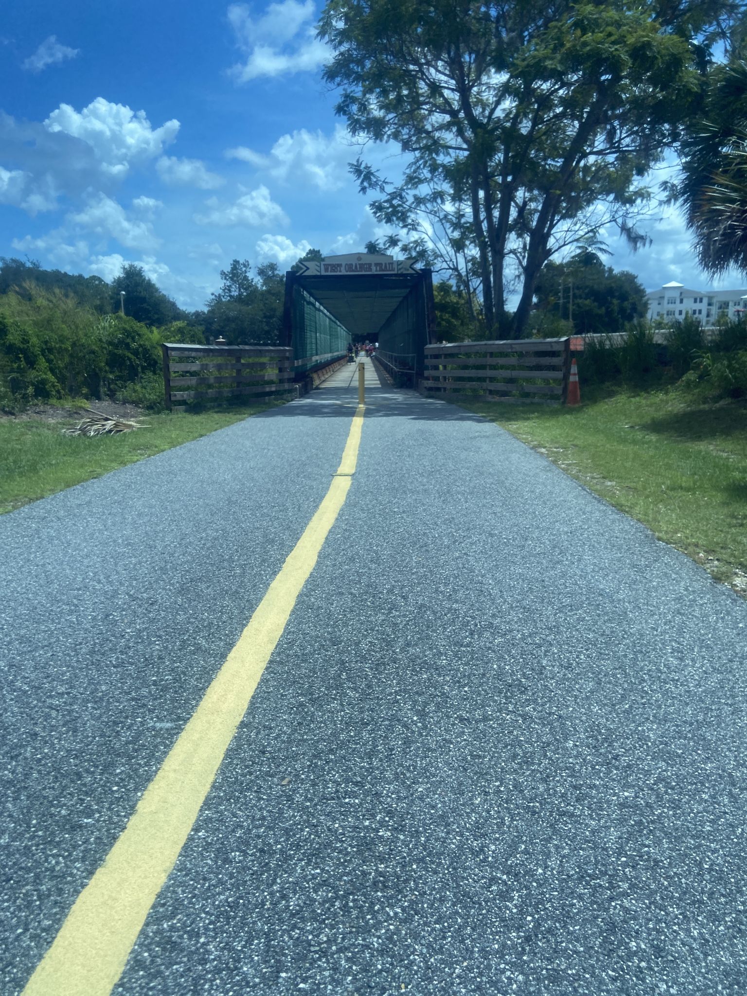 A paved path with a yellow line leads to a green metal bridge. - Lake Apopka Loop