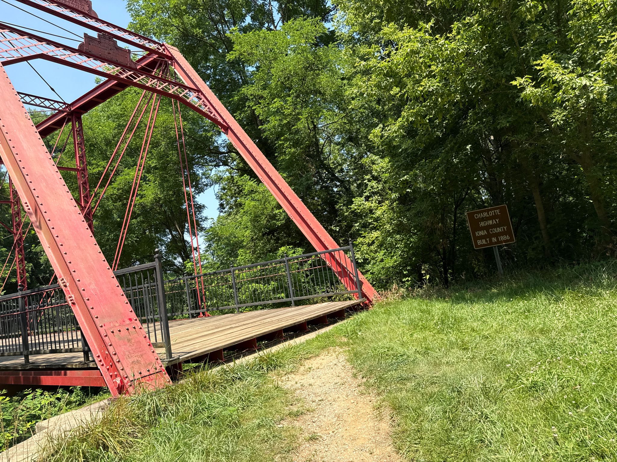 Red metal bridge viewed from a grassy path, surrounded by trees. - Historic Bridge Park, Michigan loop from Emmett Charter Township