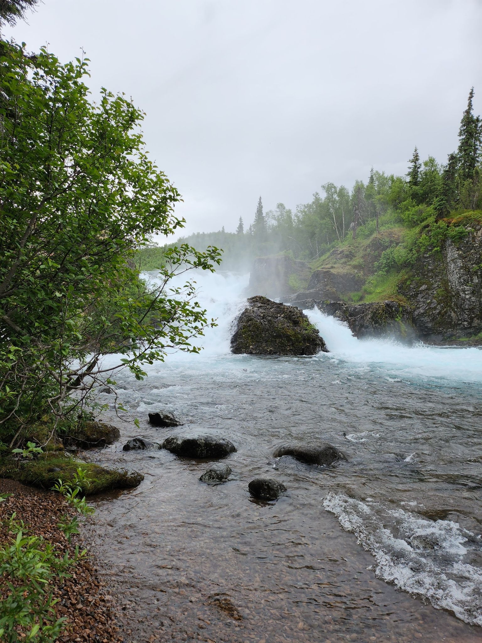 A powerful waterfall cascades over rocks in a forested river under an overcast sky. - Kontrashibuna Lake Trail