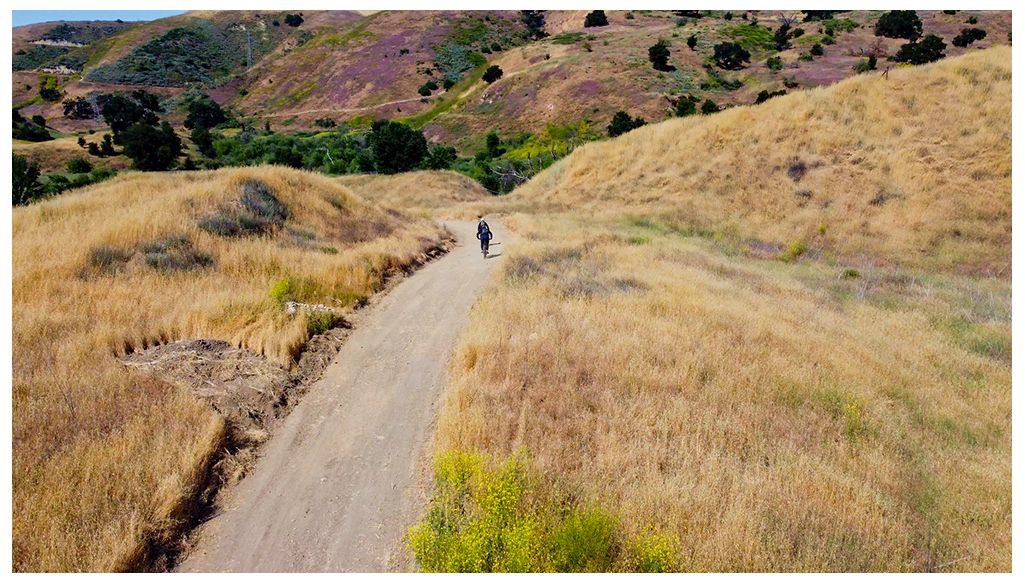 A person cycles on a dirt path through golden, dry hills. - East Las Virgenes Canyon Loop