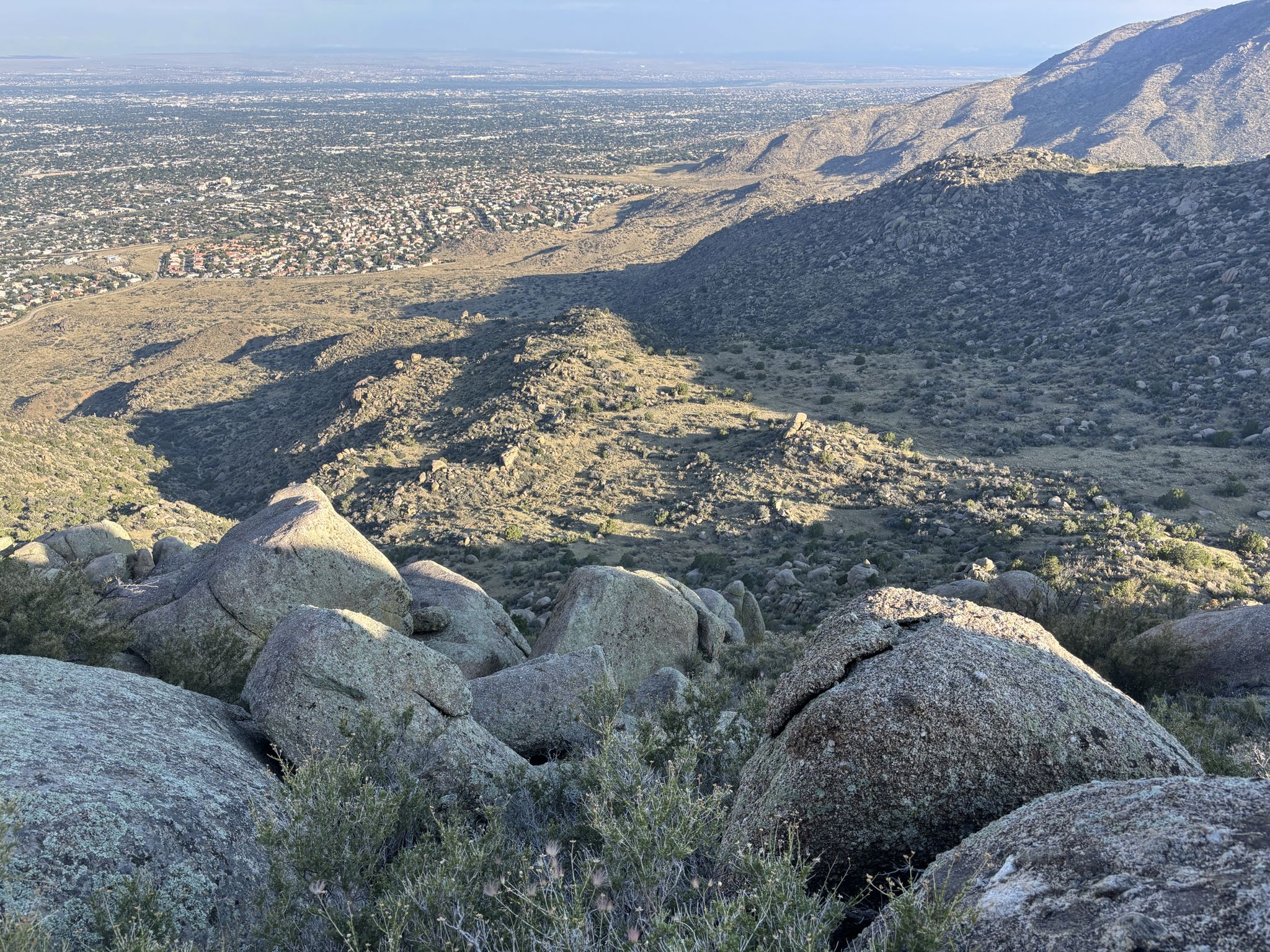 Rocky desert hillside overlooks a distant city under bright sunlight. - Eye of the Sandias Loop