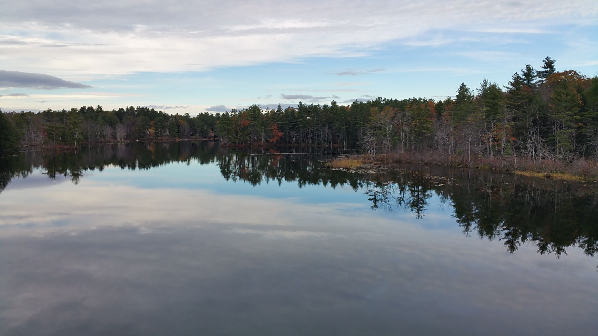 A calm lake reflects a forest under a partly cloudy sky. - Snake Pond – Mountain Division Trail loop from Little Falls