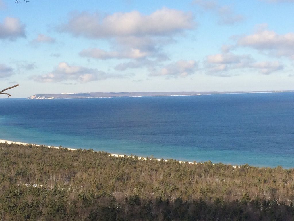 Panoramic view of a vast blue lake, distant snowy land, and a winter forest. - Alligator Hill Trail
