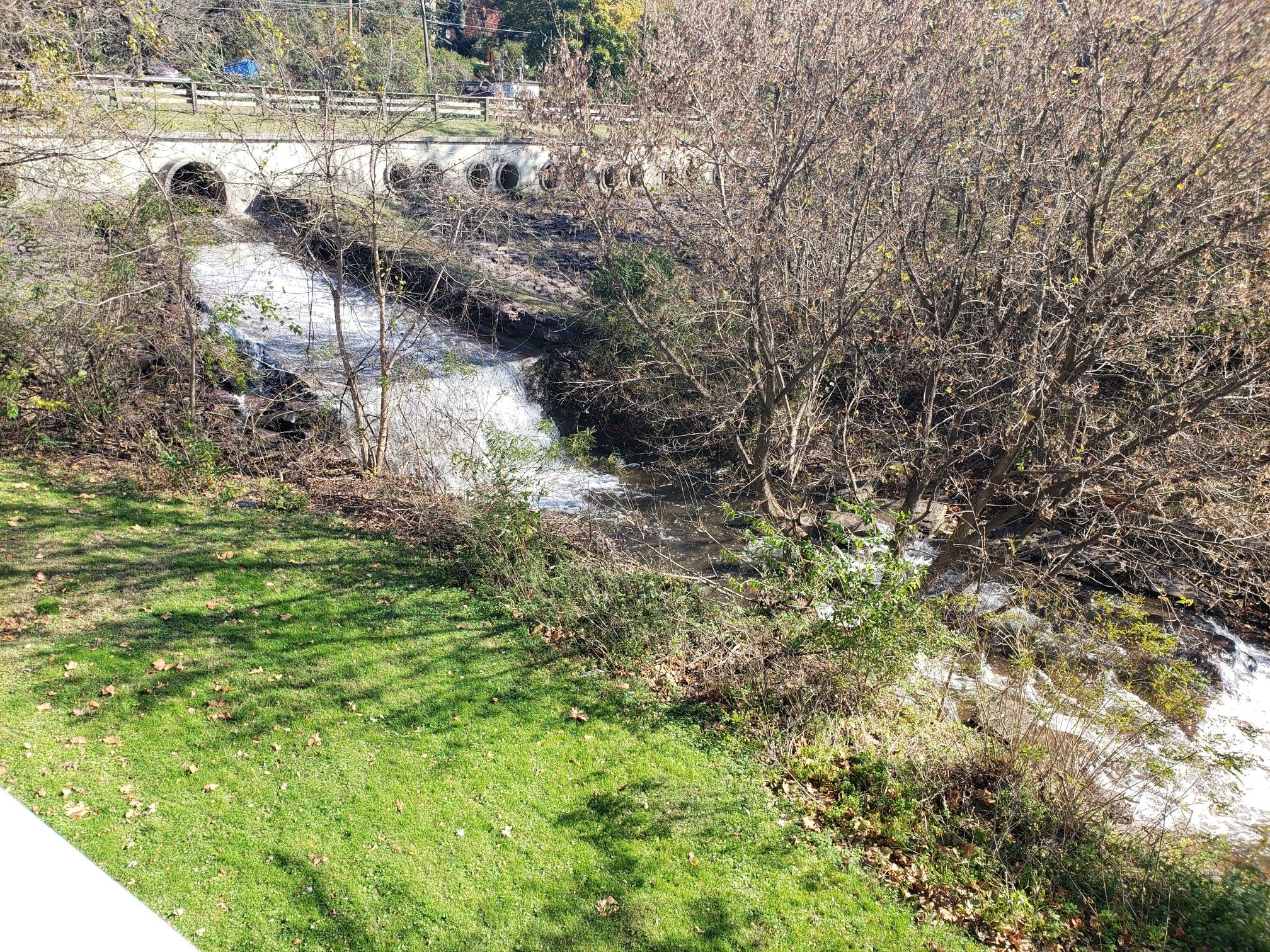 Rushing stream flows under a stone bridge, surrounded by bare trees and green grass. - Washington Crossing Bridge – Canal Bridge to the 1799 House loop from Langhorne