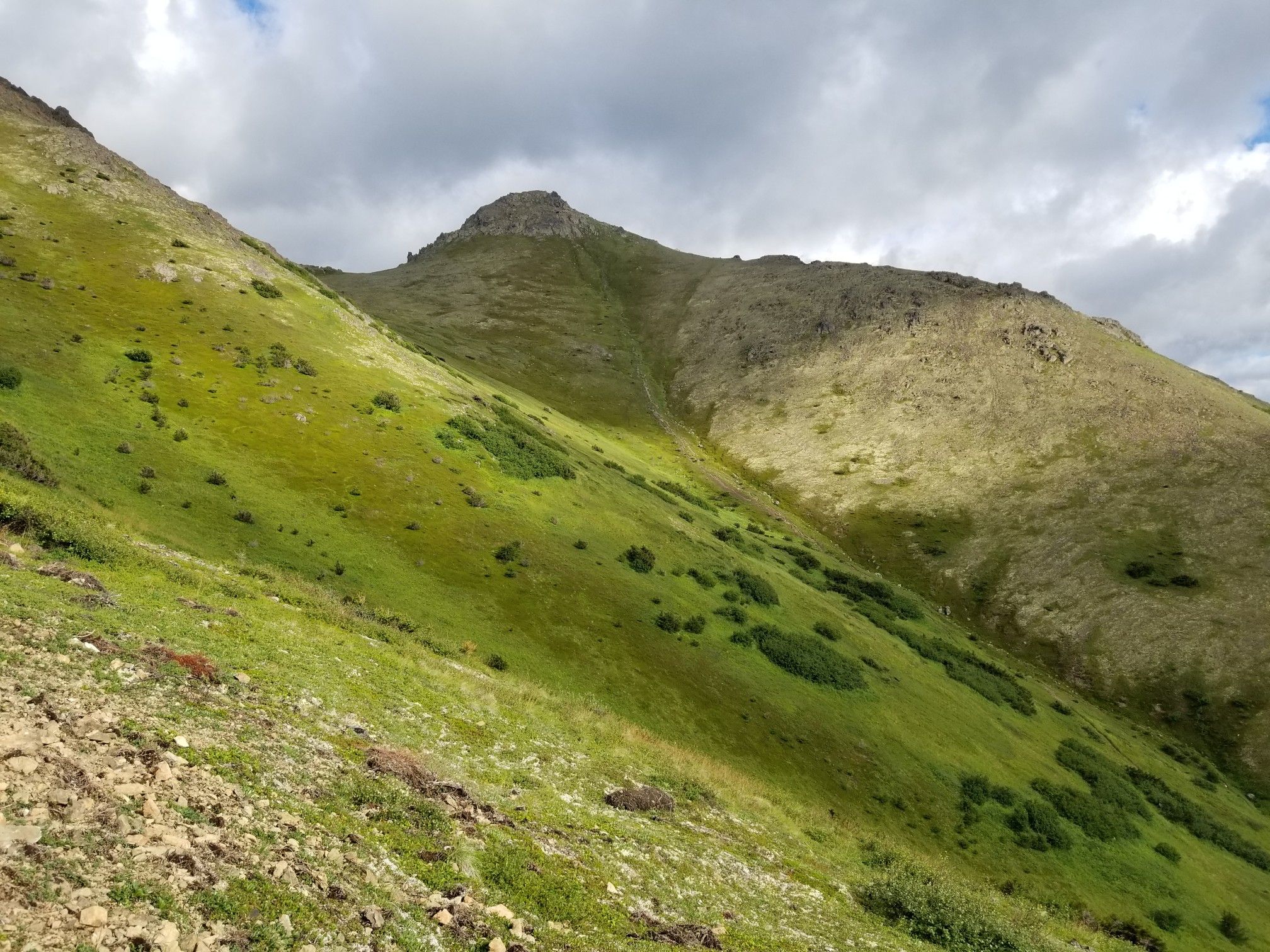 Steep, green mountain slopes under a cloudy sky with patches of sunlight. - Peak 3 and Peak 2 Loop
