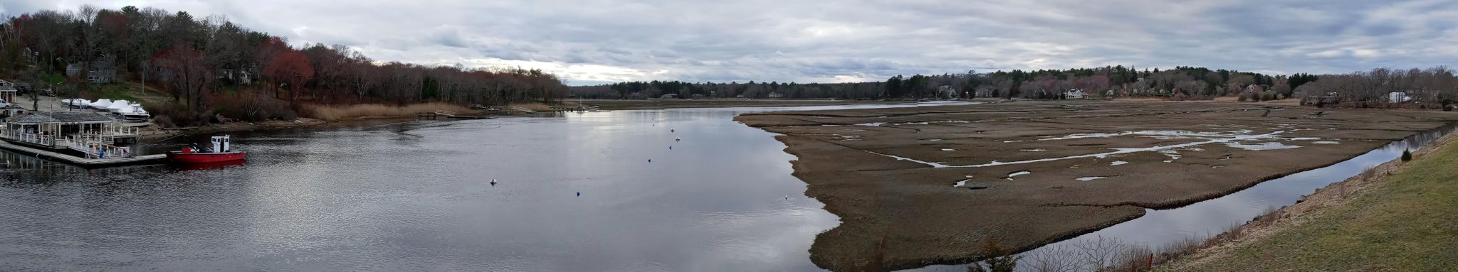 Panoramic view of a wide river next to expansive marshland under a cloudy sky. - Along the coast