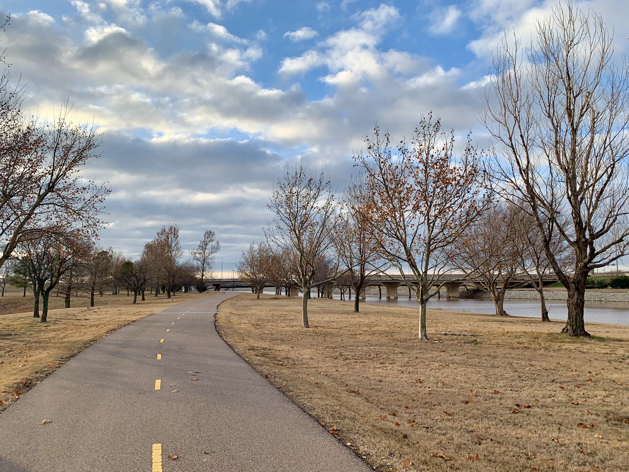 Paved path winding through bare trees beside a river on a cloudy day. - Overlook Hill loop from Six Flags Hurricane Harbor