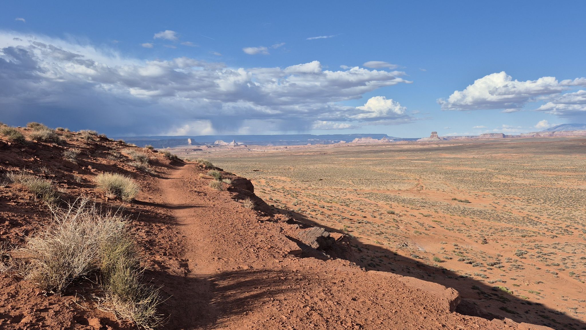A dirt path winds along a desert hillside under a partly cloudy sky. - Running loop from Page