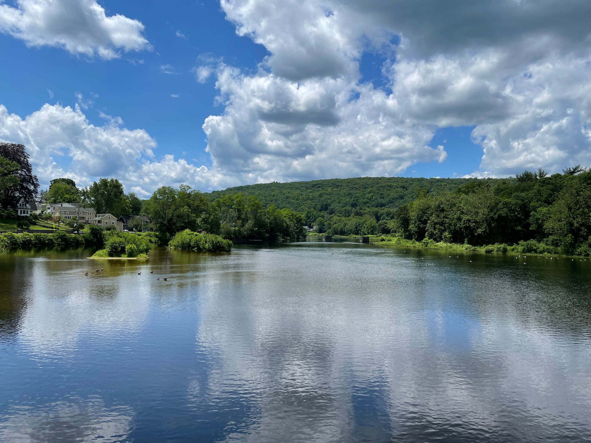 Wide lake with reflections of white clouds and green trees under a blue sky. - Seville Dam – View of the Farmington River loop from Horse Guard State Park Scenic Reserve