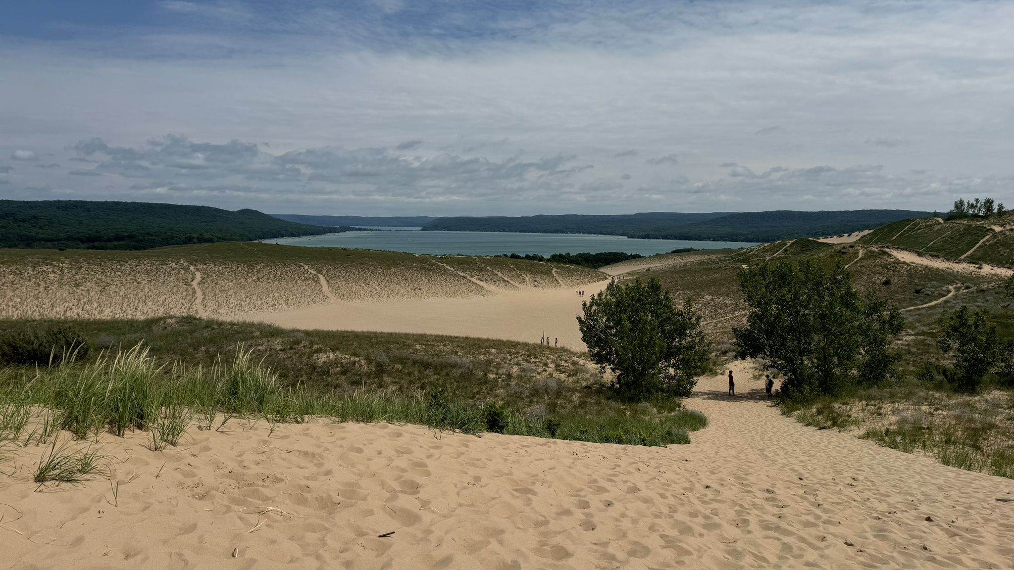 Expansive sand dunes with sparse vegetation, a distant lake, and people walking. - Dune Climb and Sleeping Bear Point Loop