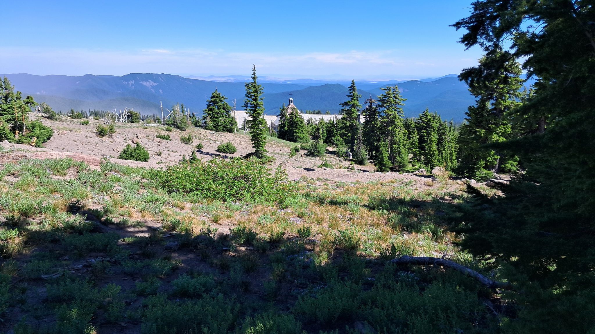 Sunny view of a distant lodge surrounded by evergreen trees and mountains. - Zigzag Canyon Overlook via Pacific Crest Trail