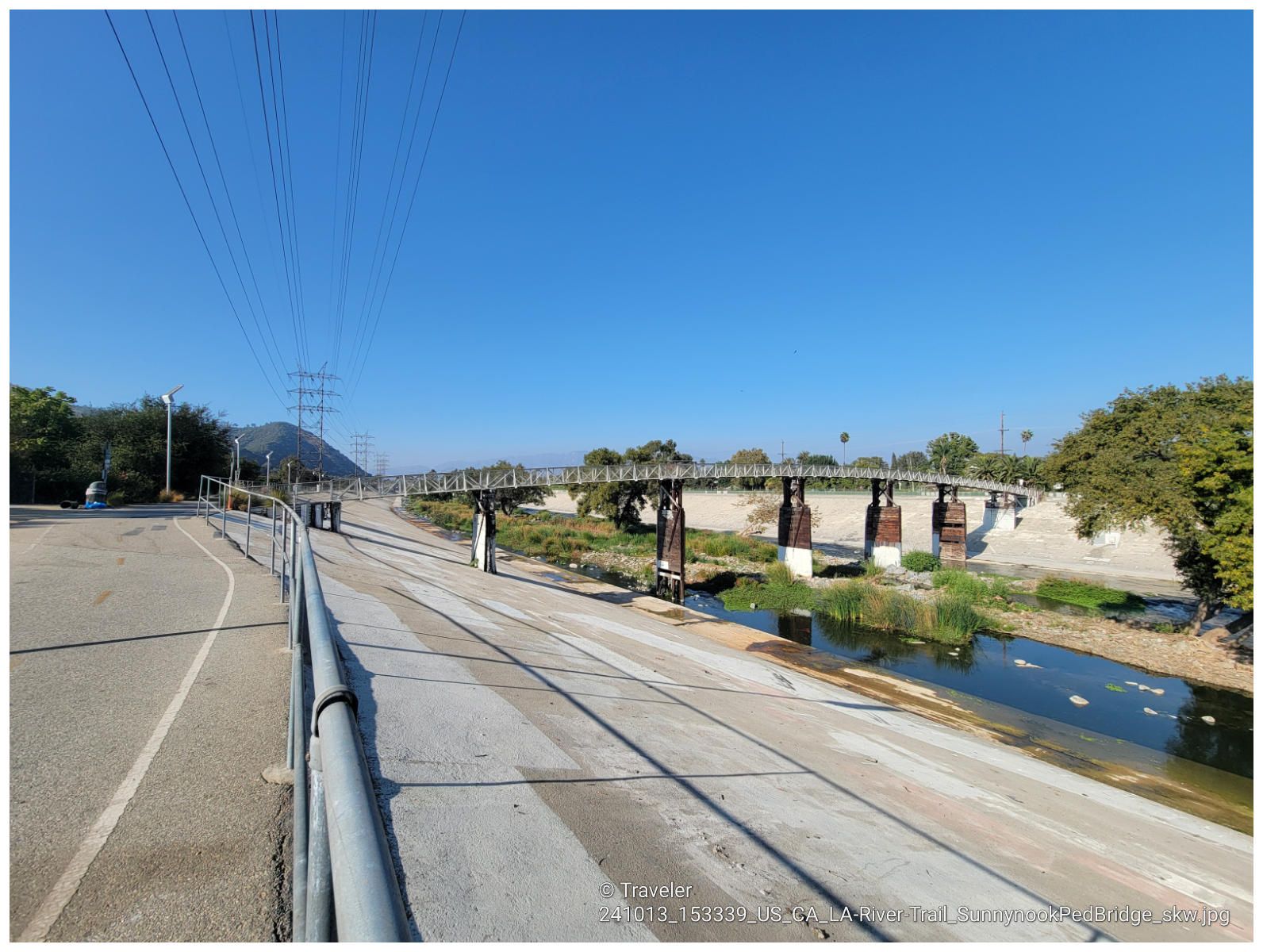 Pedestrian bridge crosses a narrow river channel under a clear blue sky. - Flint Peak Loop